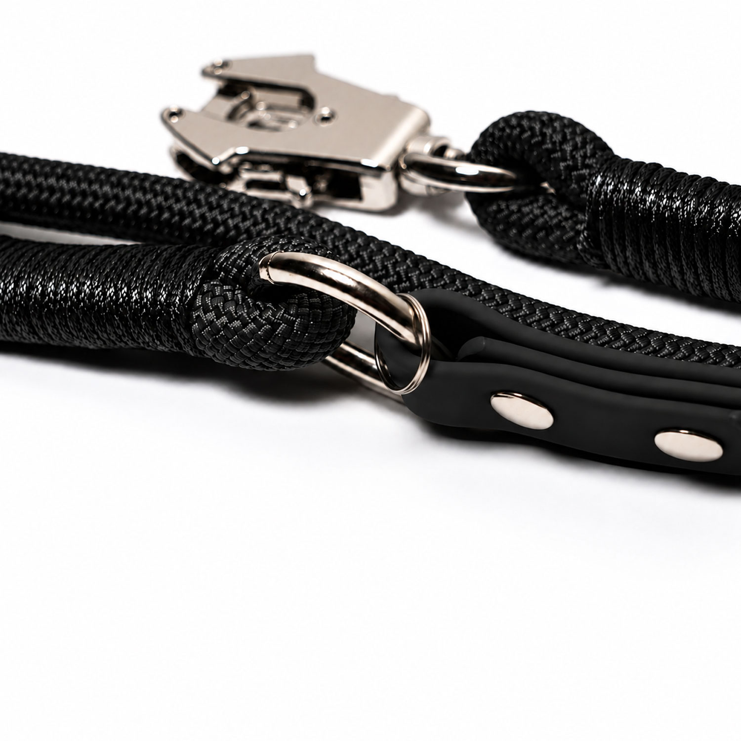 Correa para perro de cuerda de escalada negra con anillos de metal plateado y mosquetón sobre fondo blanco.