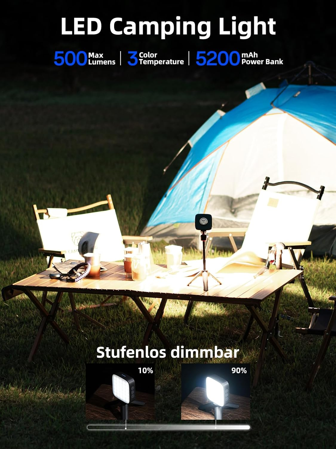 Ein Camping-Setup mit Holztisch, Stühlen und blauem Zelt im Gras, mit einer LED-Campinglampe auf einem Mini-Stativ.