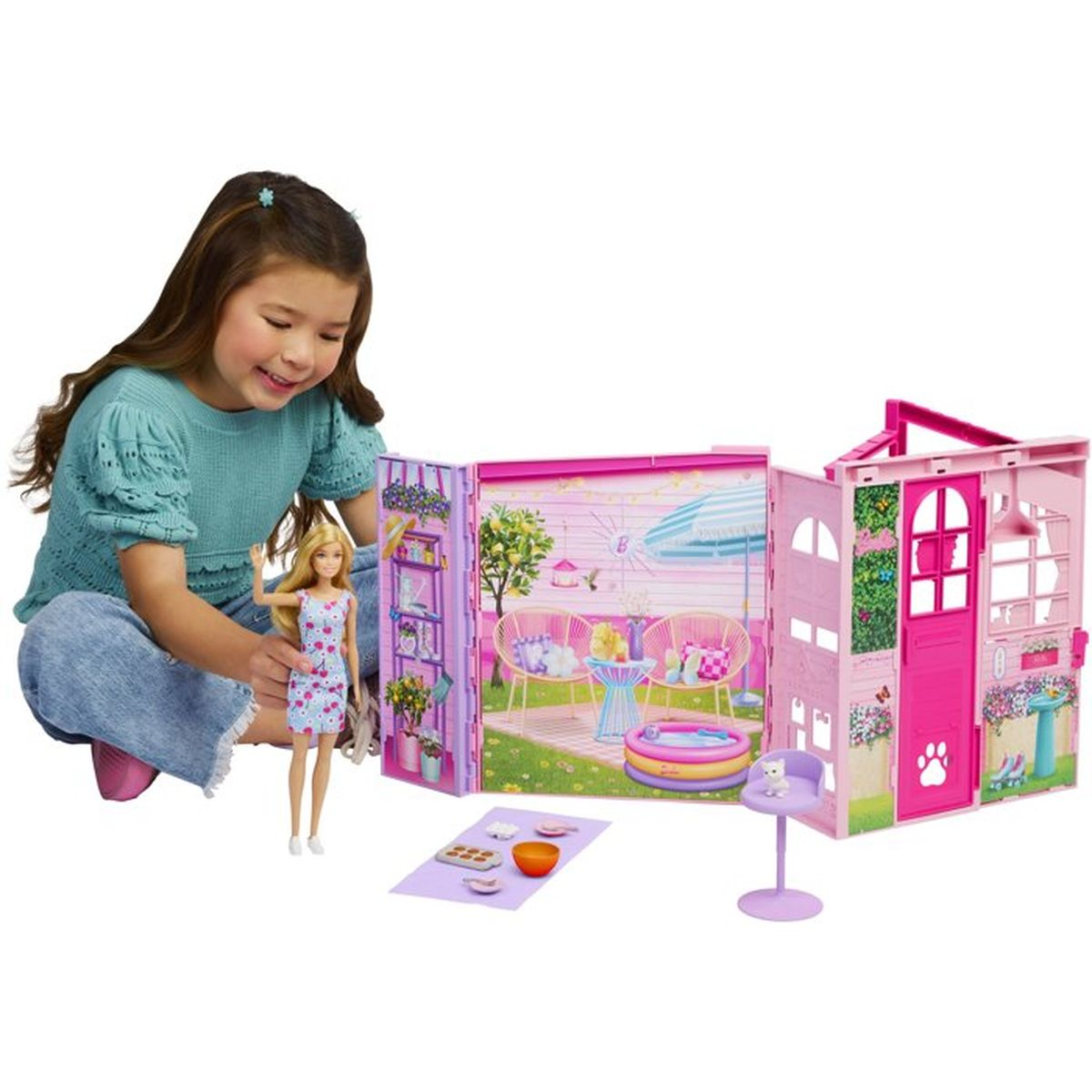 Ein lächelndes Mädchen sitzt neben einem Barbie-Puppenhaus und einer Barbie-Puppe.