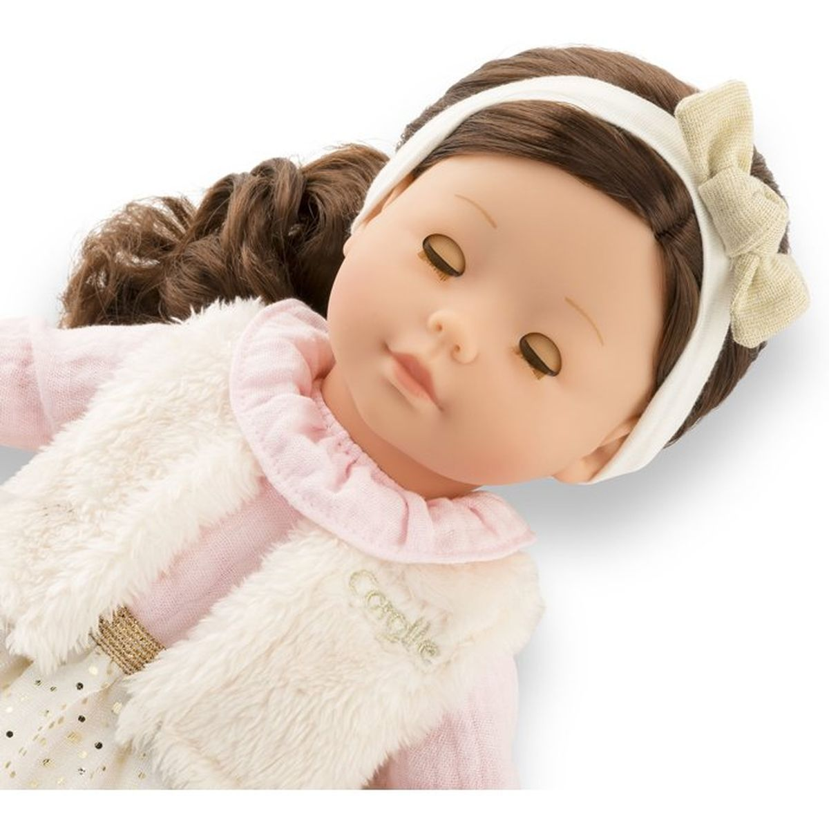 Eine Puppe mit braunem Haar, Stirnband mit Schleife, rosa Oberteil und weißer Fellweste.