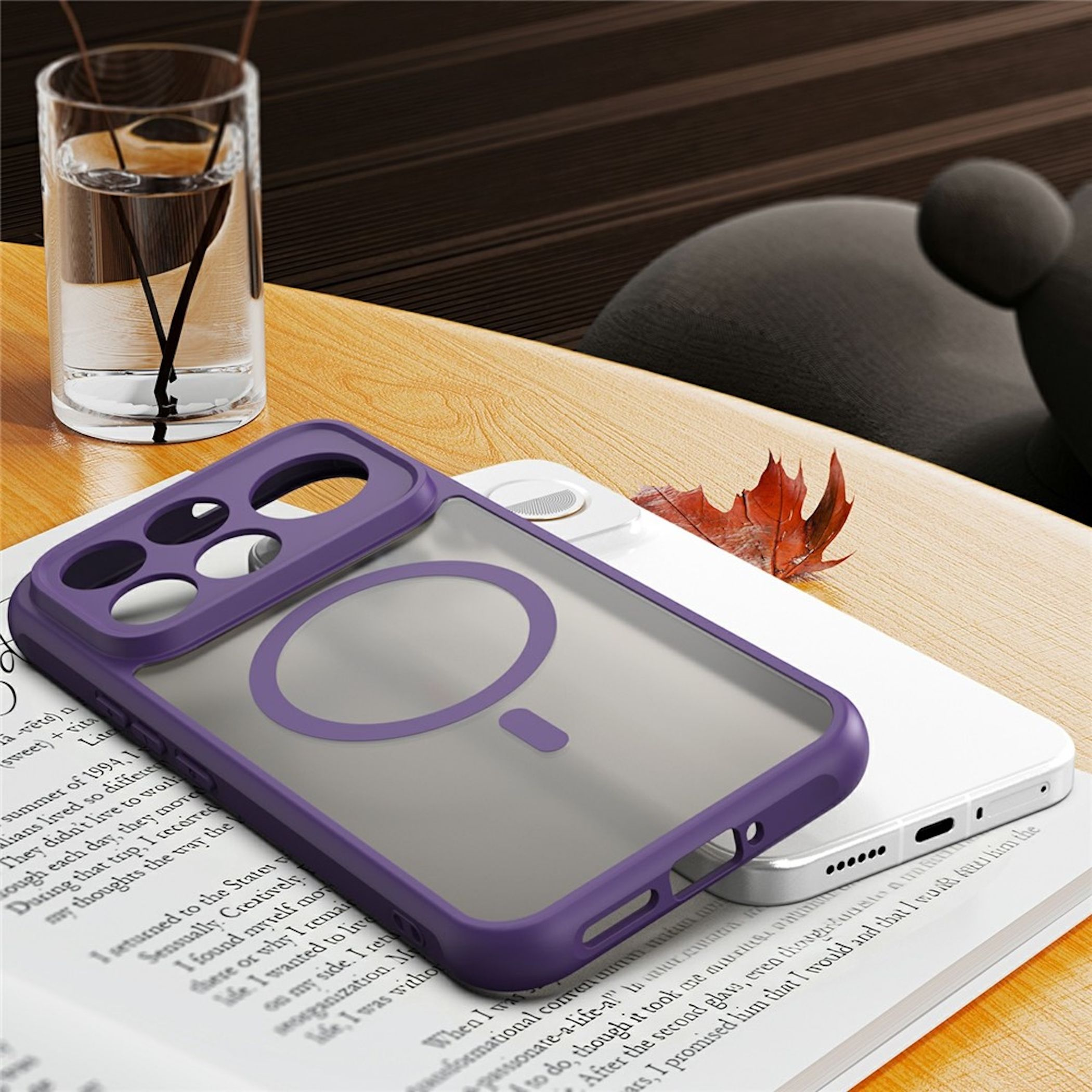 Eine lila Smartphone-Hülle liegt auf einem Buch, daneben ein Glas Wasser und ein trockenes Blatt.