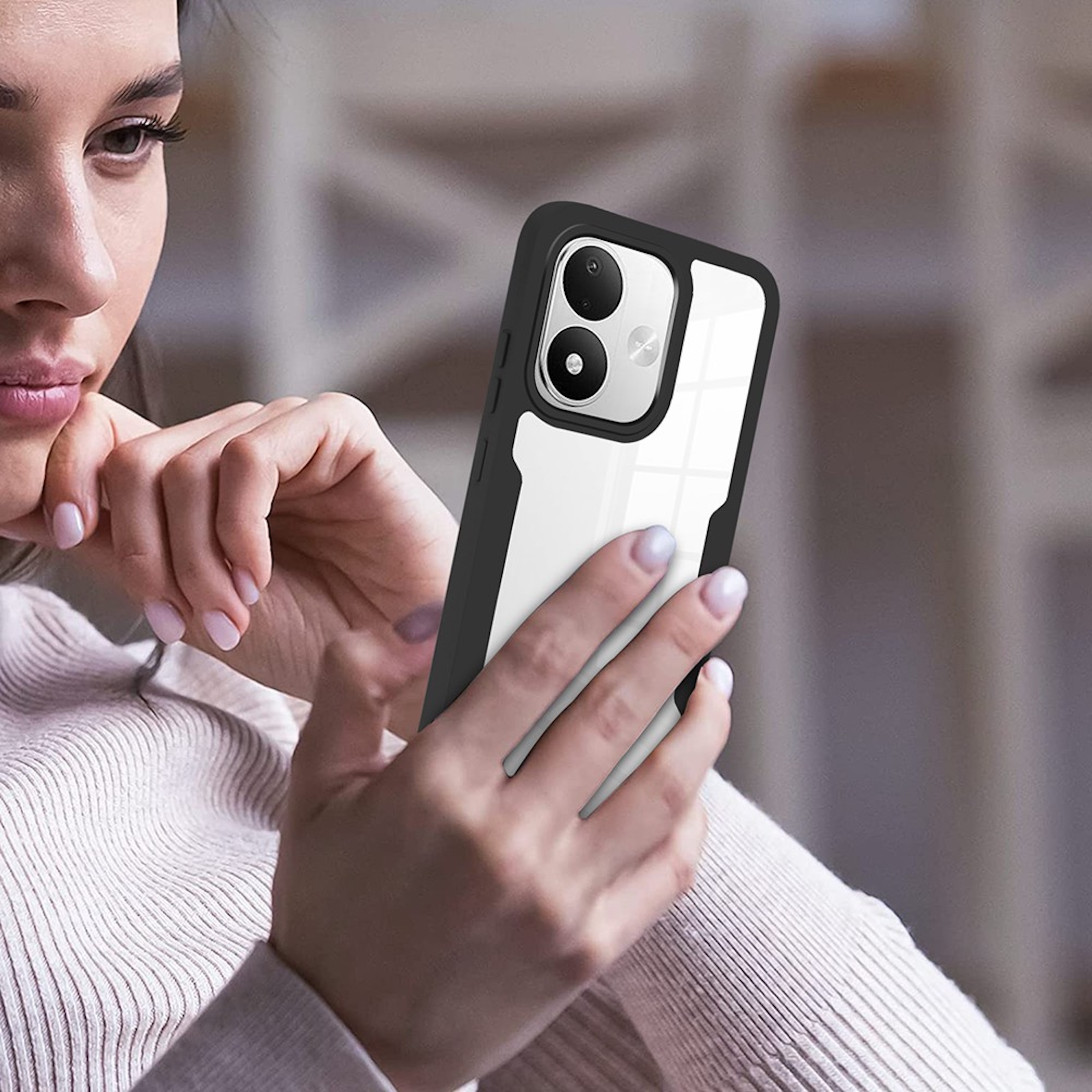 Eine Frau in einem beigen Pullover hält ein Smartphone mit schwarzer Hülle und klarer Rückseite.