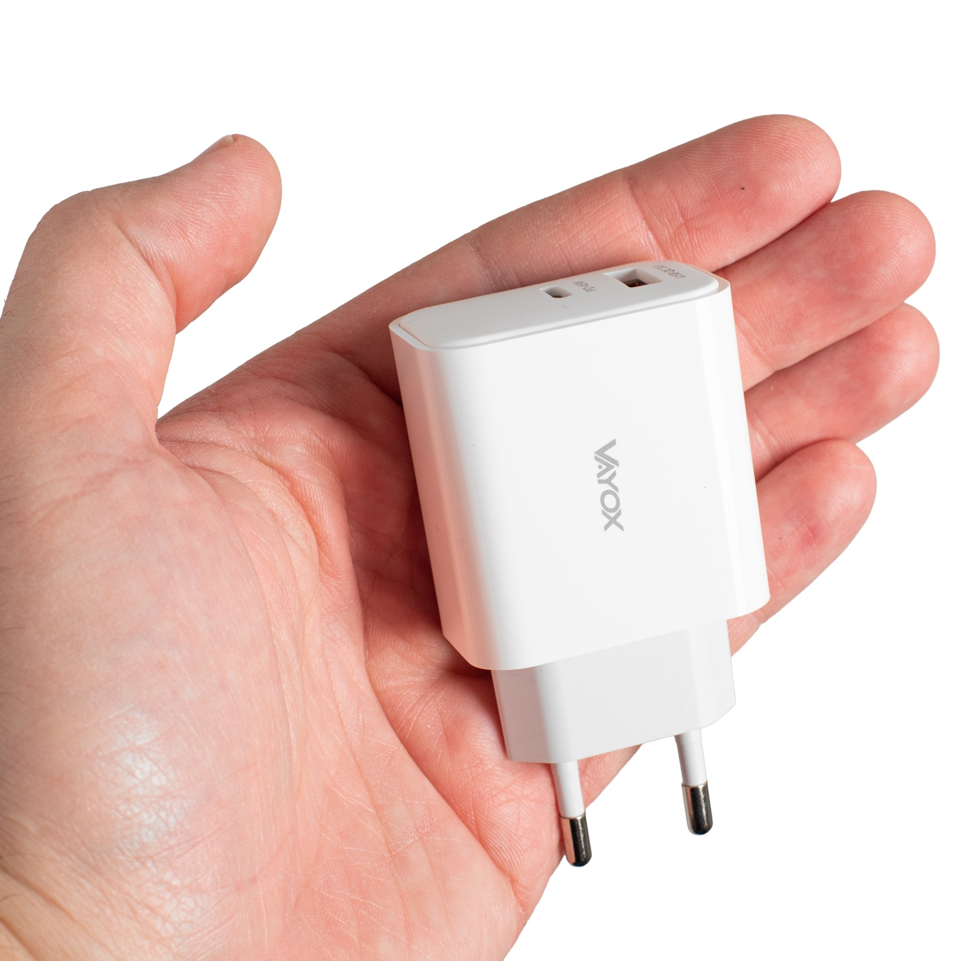 Egy fehér Vayox töltő két USB-porttal egy nyitott tenyéren fekszik, fehér háttér előtt.