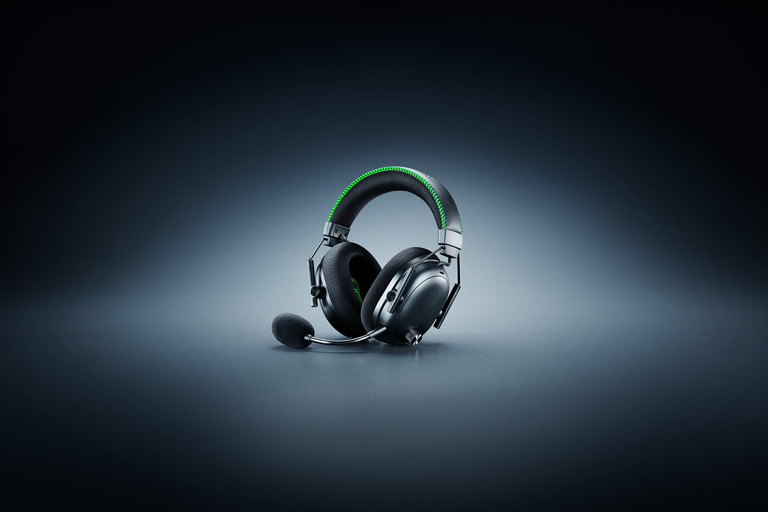 Schwarzes Gaming-Headset mit grünem Rand und Mikrofon auf grauem Untergrund vor dunklem Hintergrund.