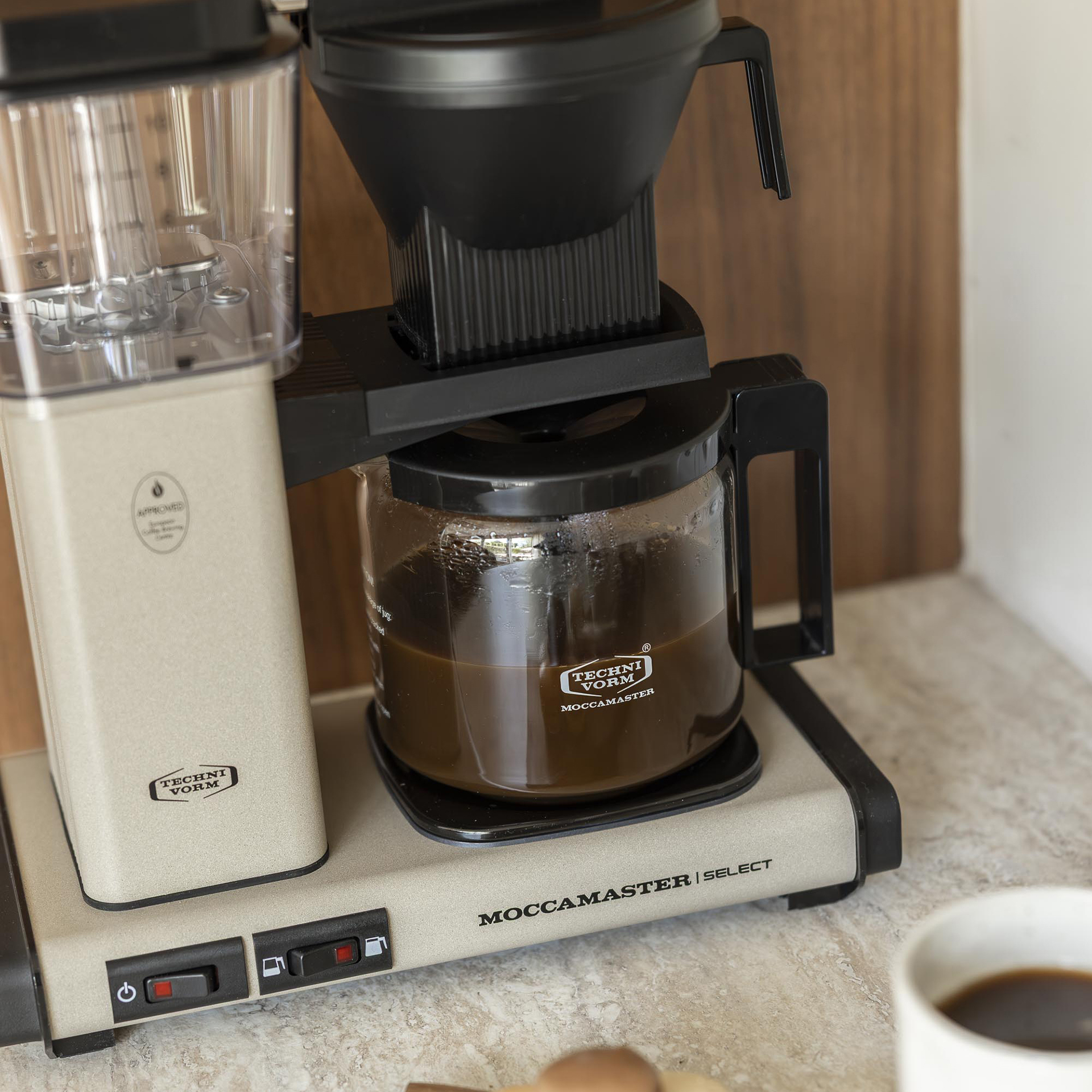 Une cafetière Technivorm Moccamaster beige posée sur un comptoir de cuisine avec du café fraîchement infusé.