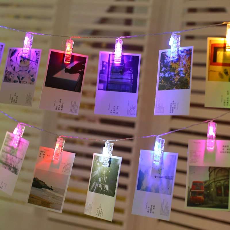 Polaroid-Fotos an zwei leuchtenden Lichterketten mit bunten LED-Clips vor einer Holzwand.