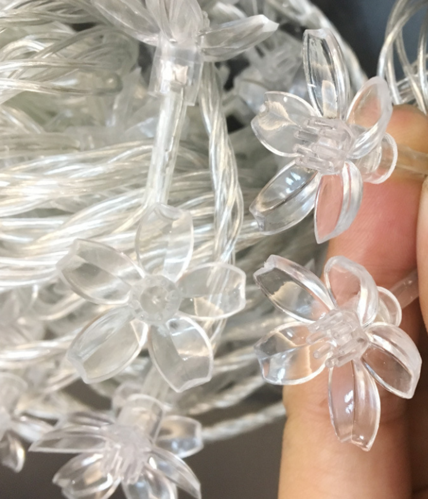 Transparente, blütenförmige Aufsätze auf einer Lichterkette, gehalten von einer Hand.
