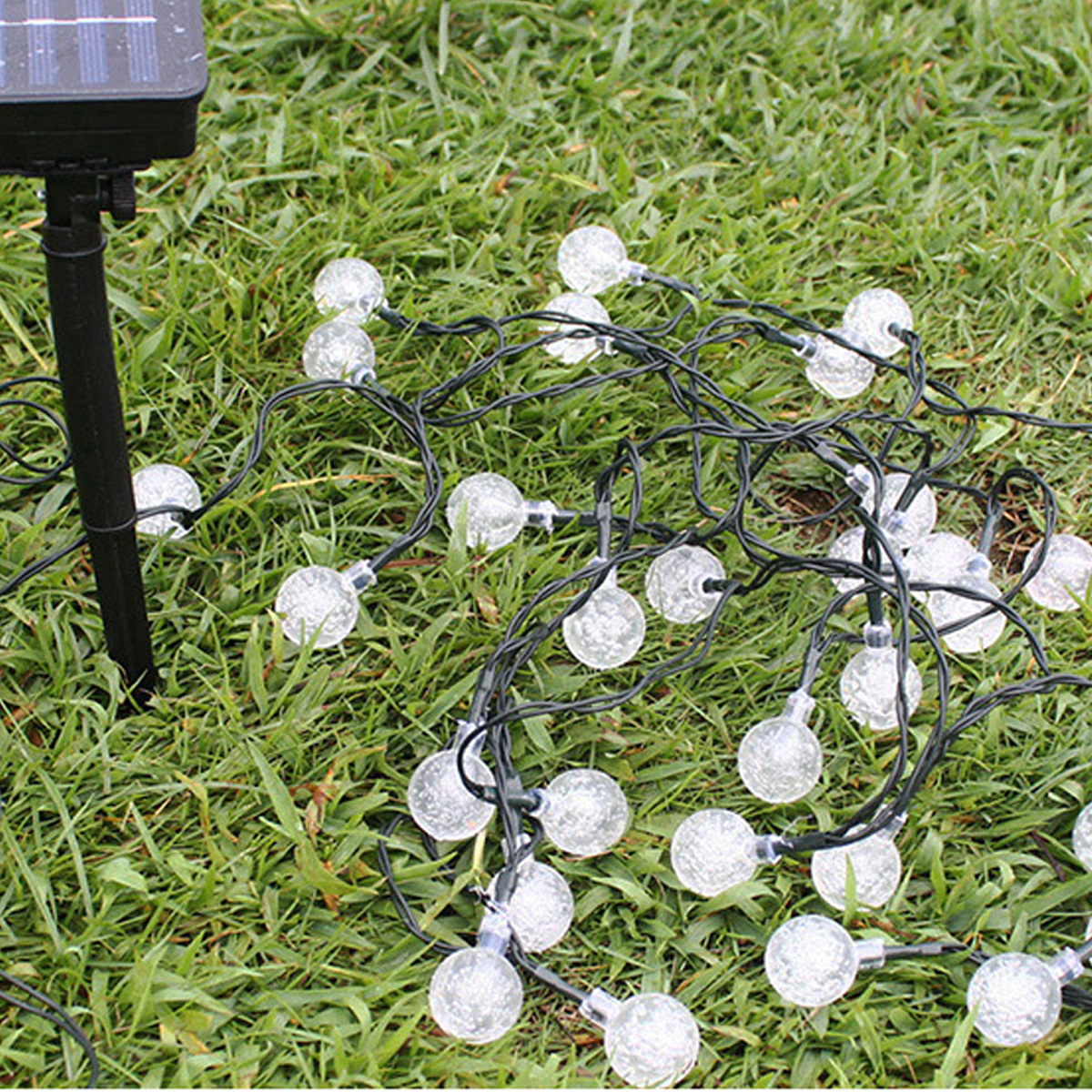Solar-Lichterkette mit gläsernen Kugeln auf grünem Gras neben einem Solarpanel.