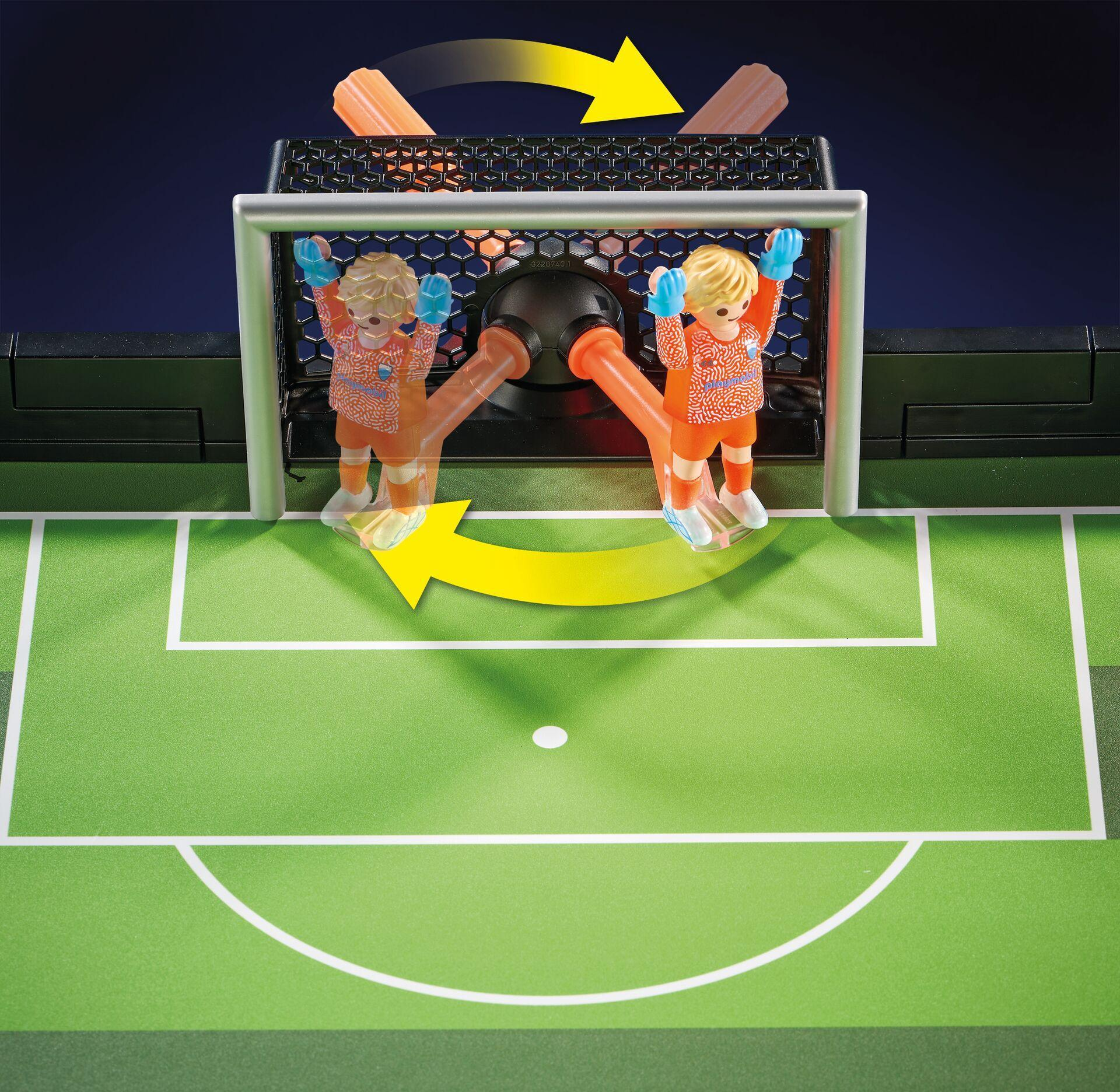 Figuras de portero de Playmobil en barras giratorias frente a un campo de fútbol verde con flechas amarillas.