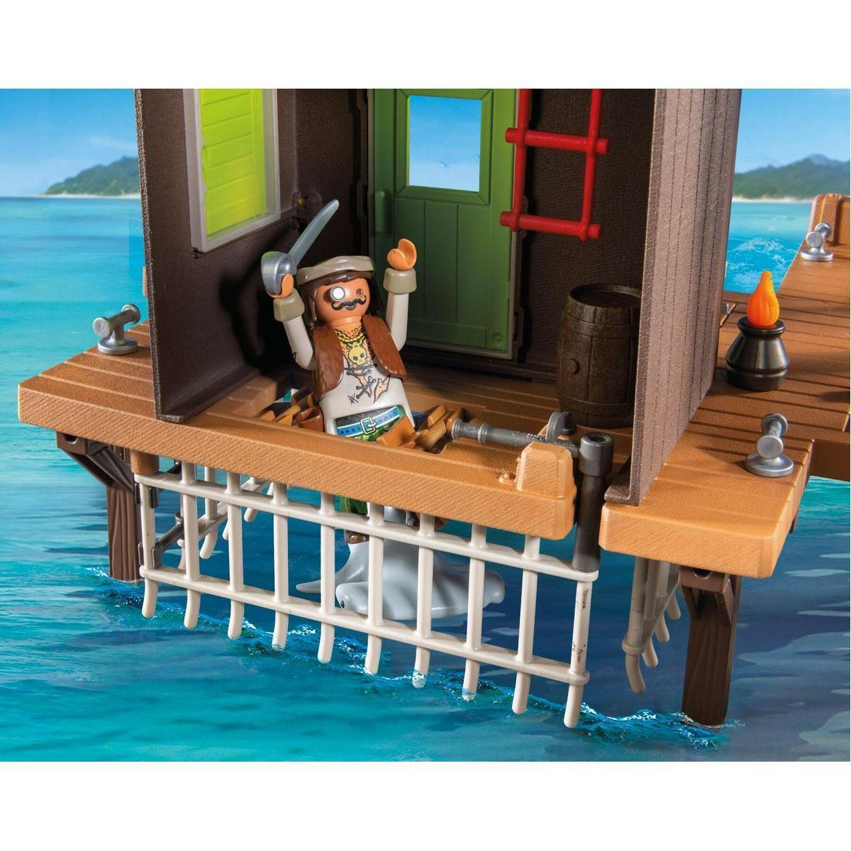 Figurine de pirate Playmobil sur un jetée en bois sur l'eau, avec tonneau, torche et cage blanche en bas.