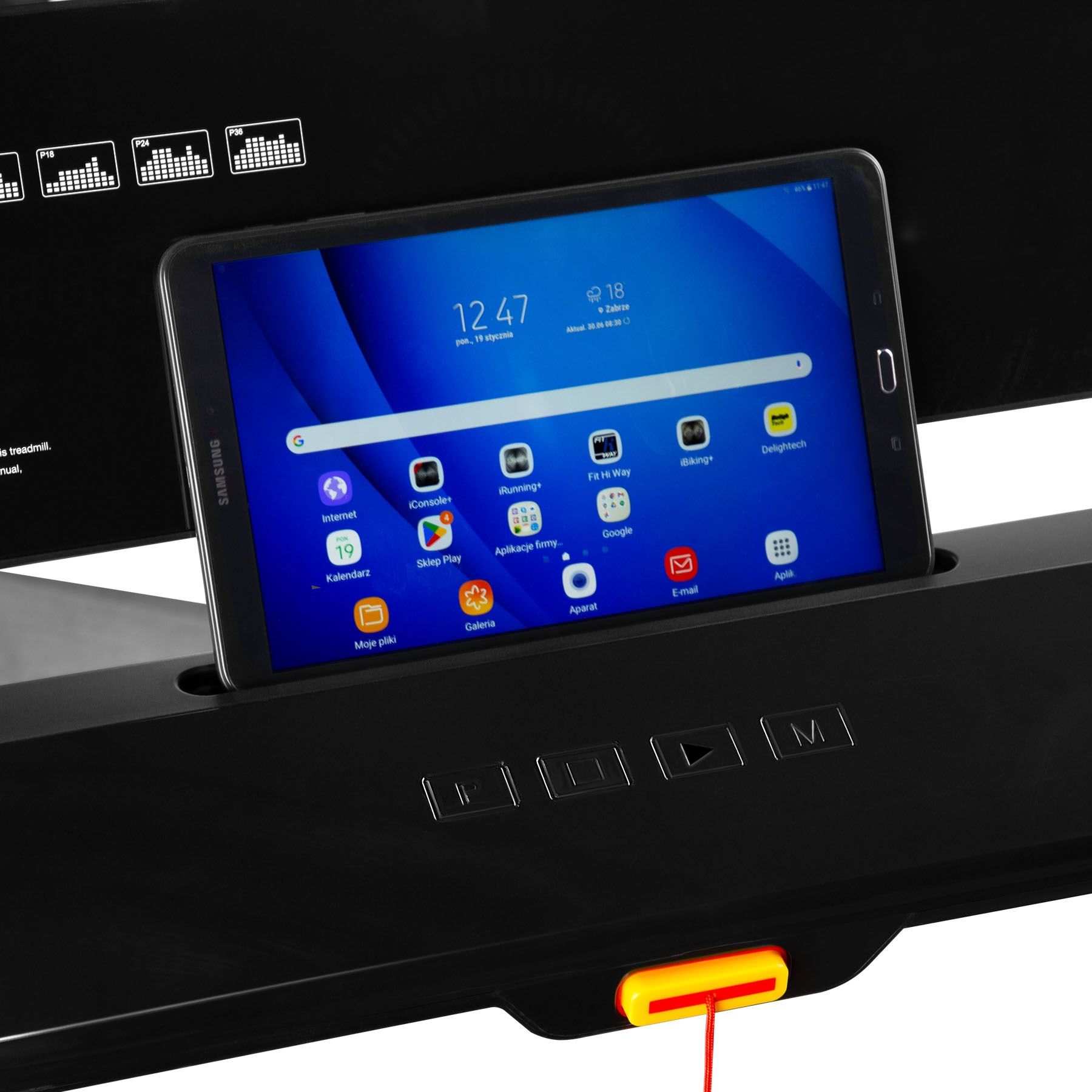 Tablet Samsung z ikonami aplikacji i godziną spoczywa na konsoli bieżni.
