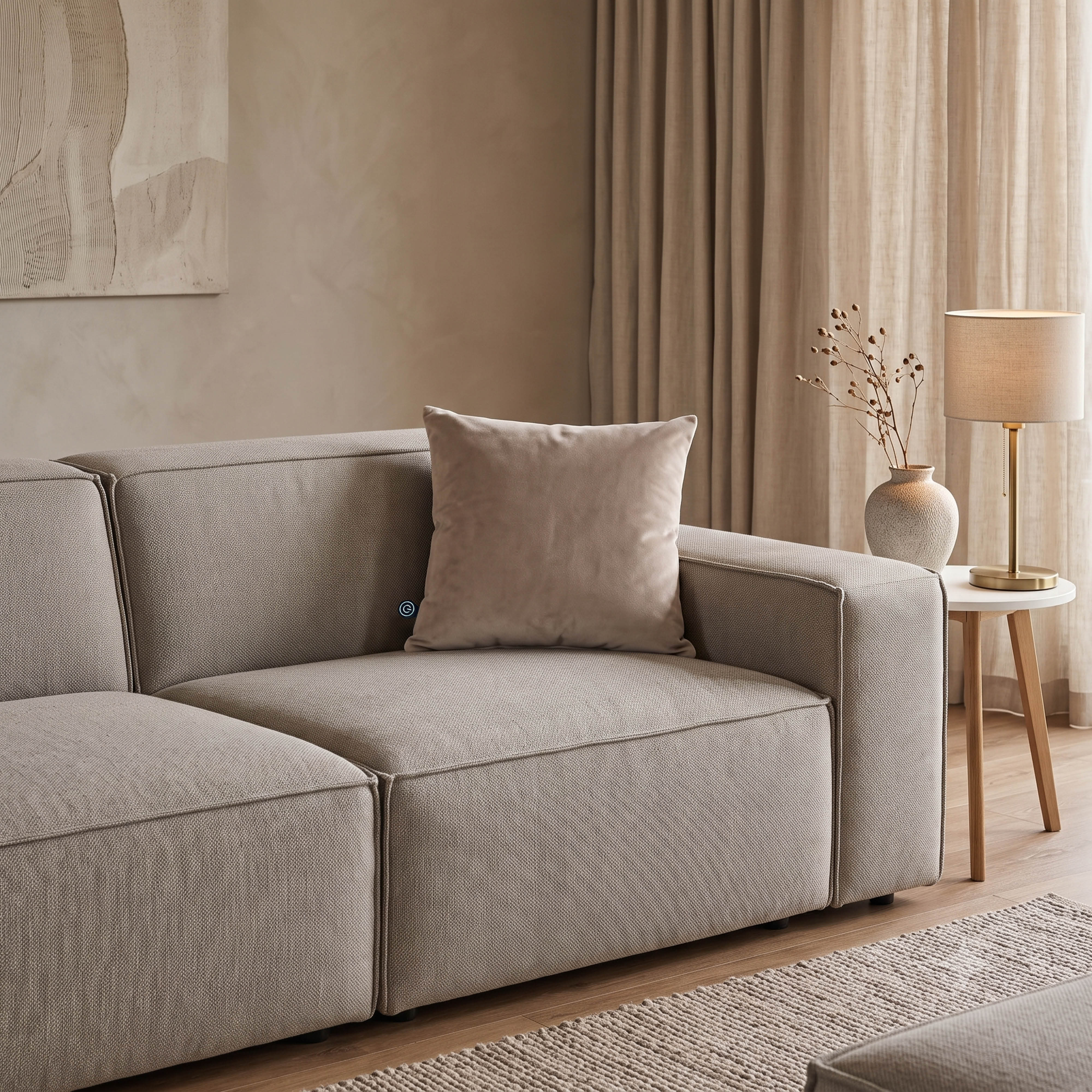 Un canapé beige confortable avec un coussin dans un salon moderne avec lampe et rideaux neutres.