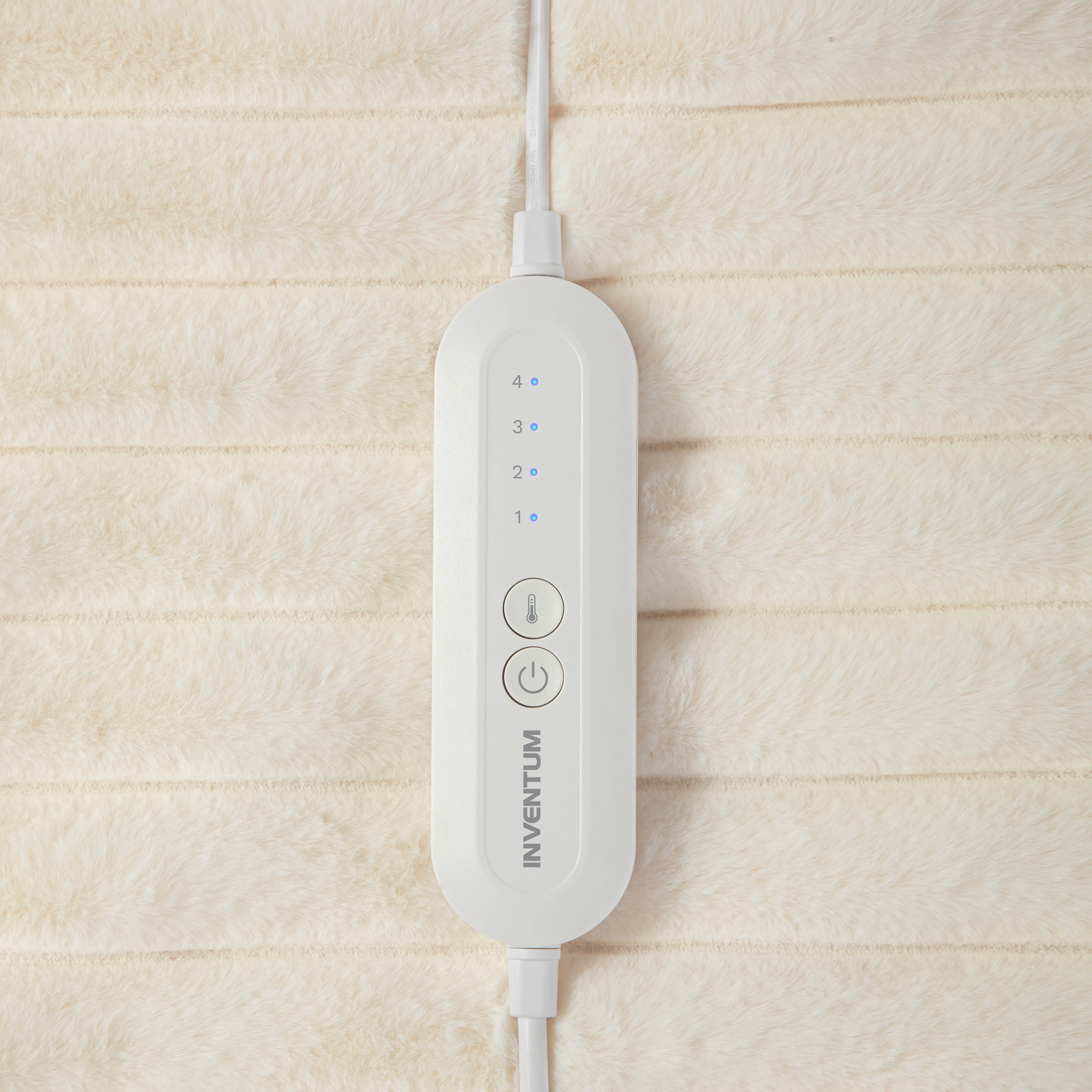 Un contrôleur de coussin chauffant blanc avec quatre réglages et deux boutons sur un tissu pelucheux crème.