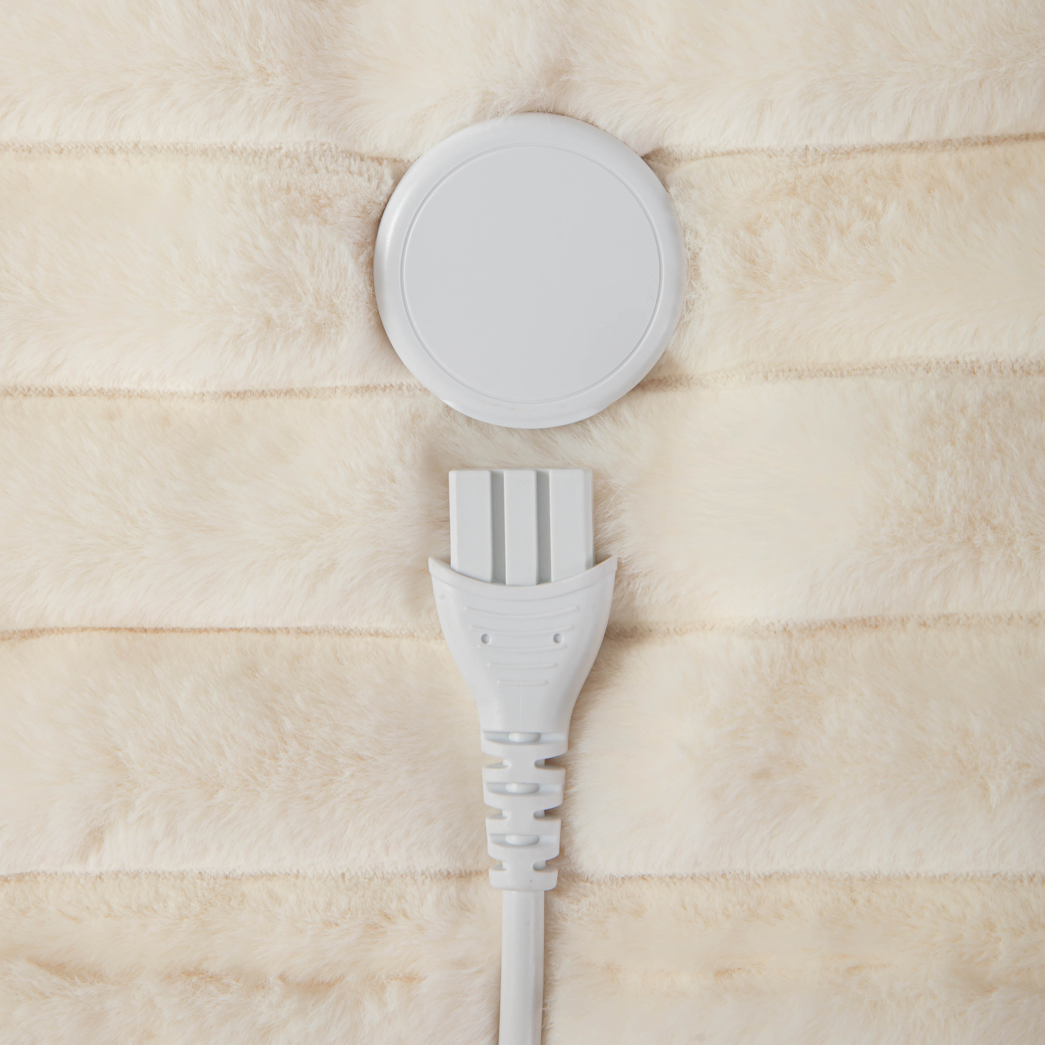 Un chargeur sans fil rond blanc et une prise sur une couverture de couleur crème.