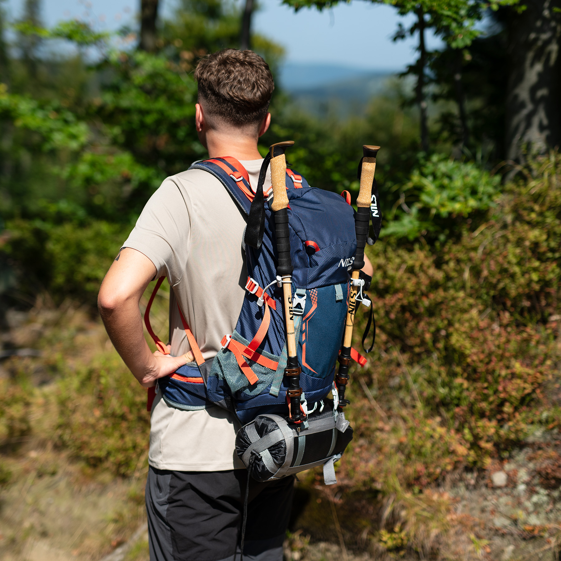 Wędrowiec z niebieskim plecakiem i kijkami trekkingowymi w lesie.