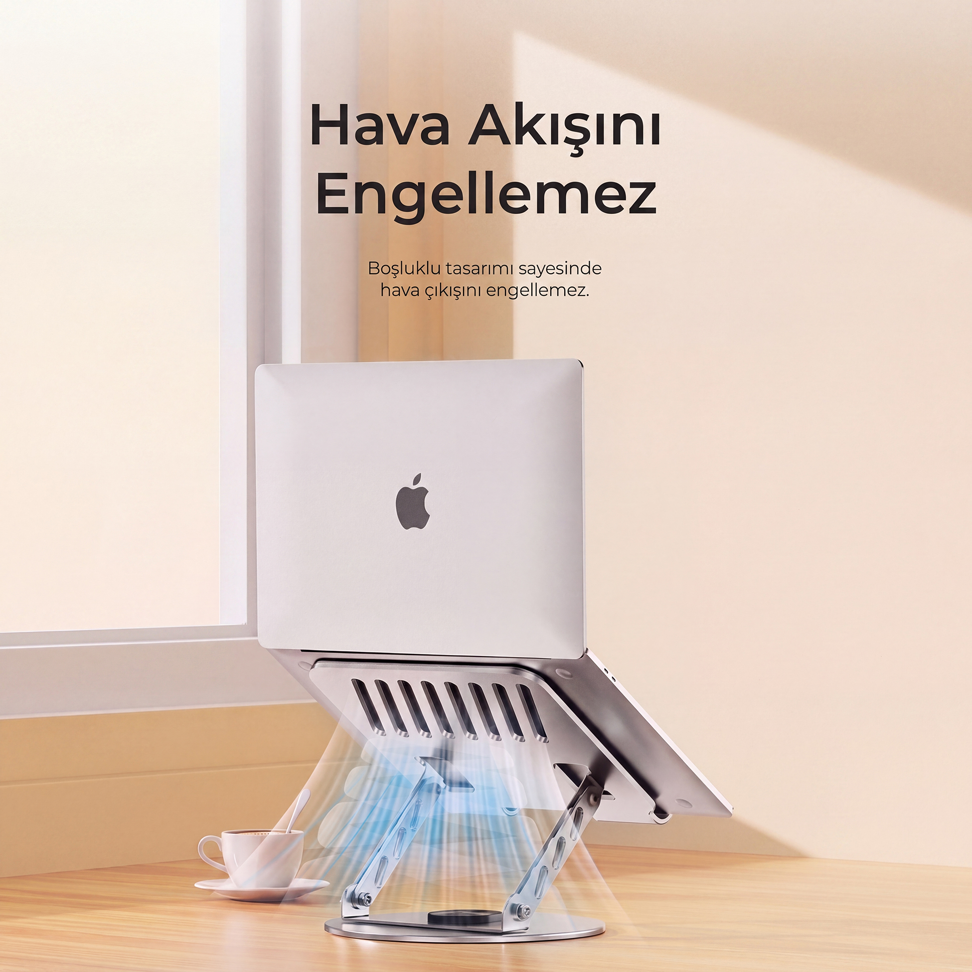 Ahşap masa üzerinde havalandırma delikli gümüş renkli laptop standı, arka planda pencere var.