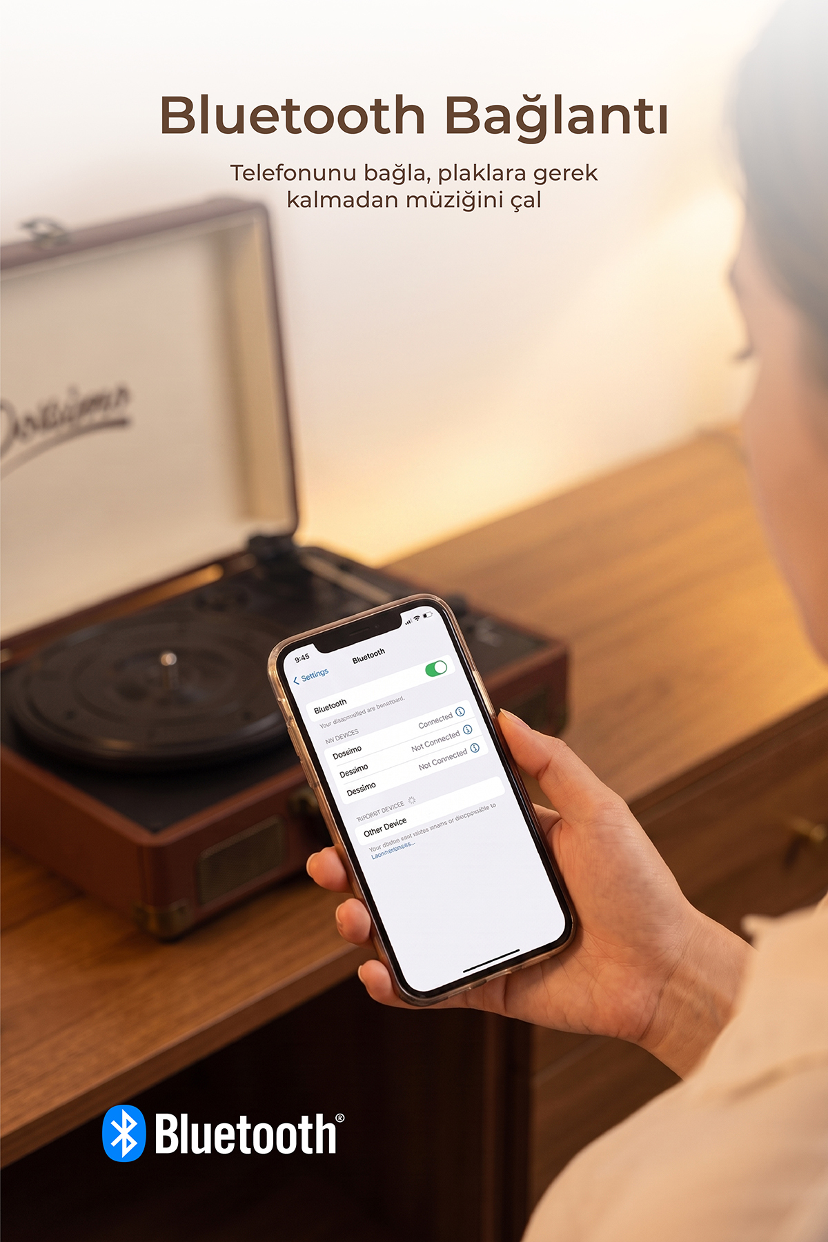 Bir kişi Bluetooth ayarlarını gösteren telefon tutuyor, arkada ahşap masa üzerinde nostaljik bir plakçalar var.
