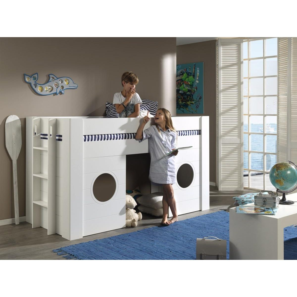 Zwei Kinder im kinderzimmer mit einem weißen hochbett im schiff design, einer blauen matte und meerblick.