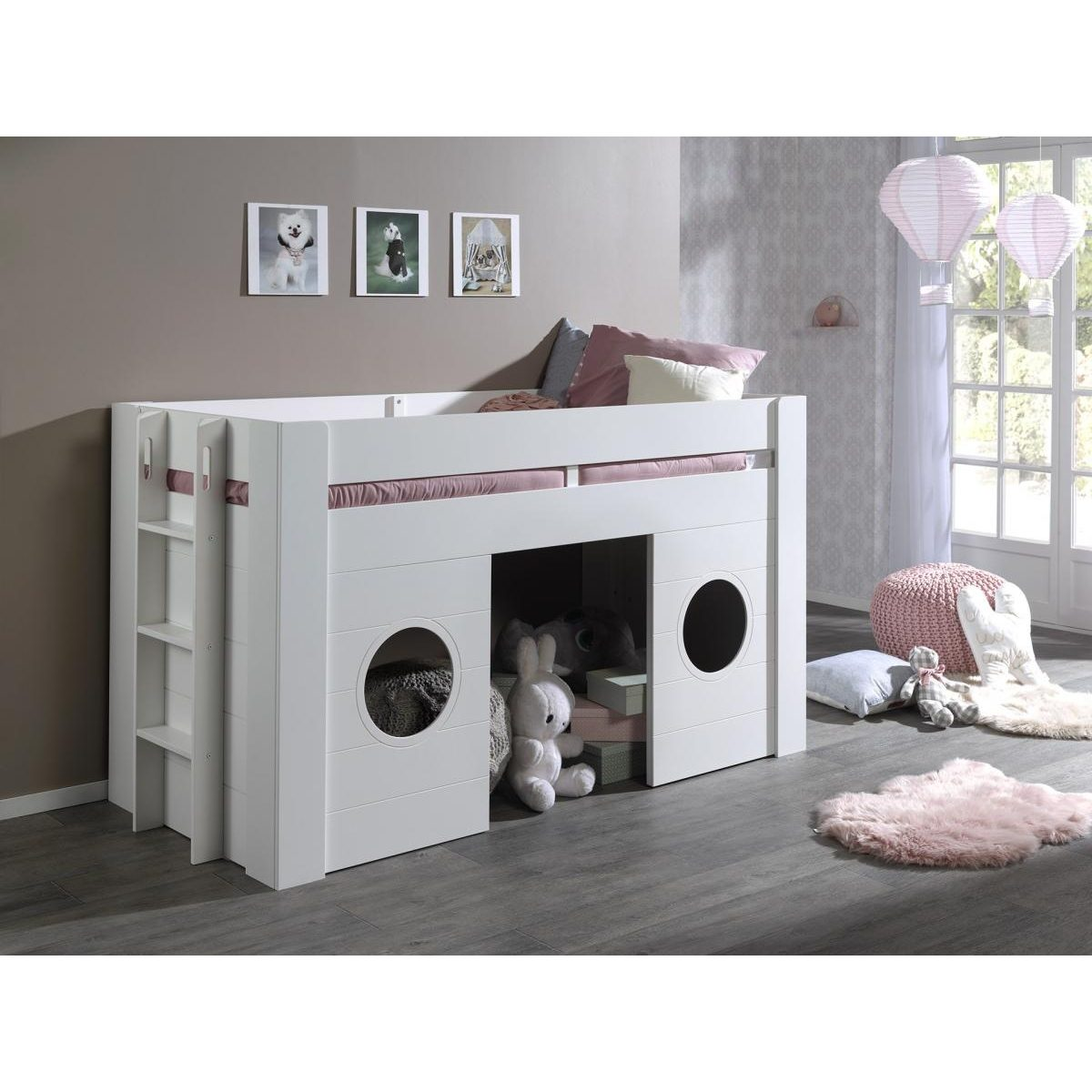 Ein weißes Hochbett mit Spielhaus unten, runden Fenstern, Kissen und Kuscheltieren in einem Zimmer.