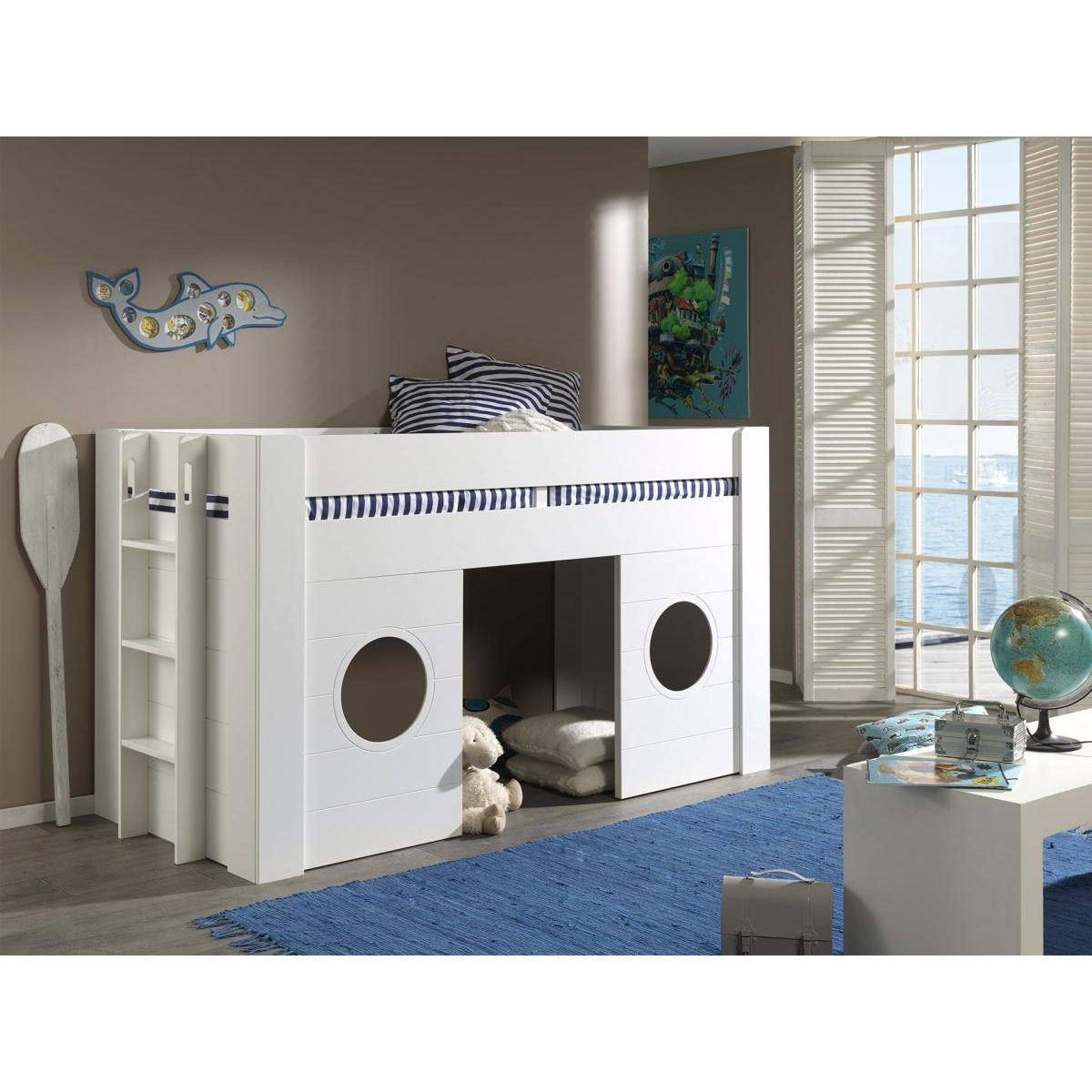 Ein weißes Kinderbett im Schiffsdesign mit Leiter, Bullaugen und blauem Teppich im hellen Zimmer.