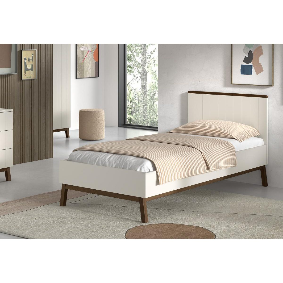 Ein weißes Einzelbett mit Holzbeinen steht in einem hellen Schlafzimmer auf einem runden Teppich.