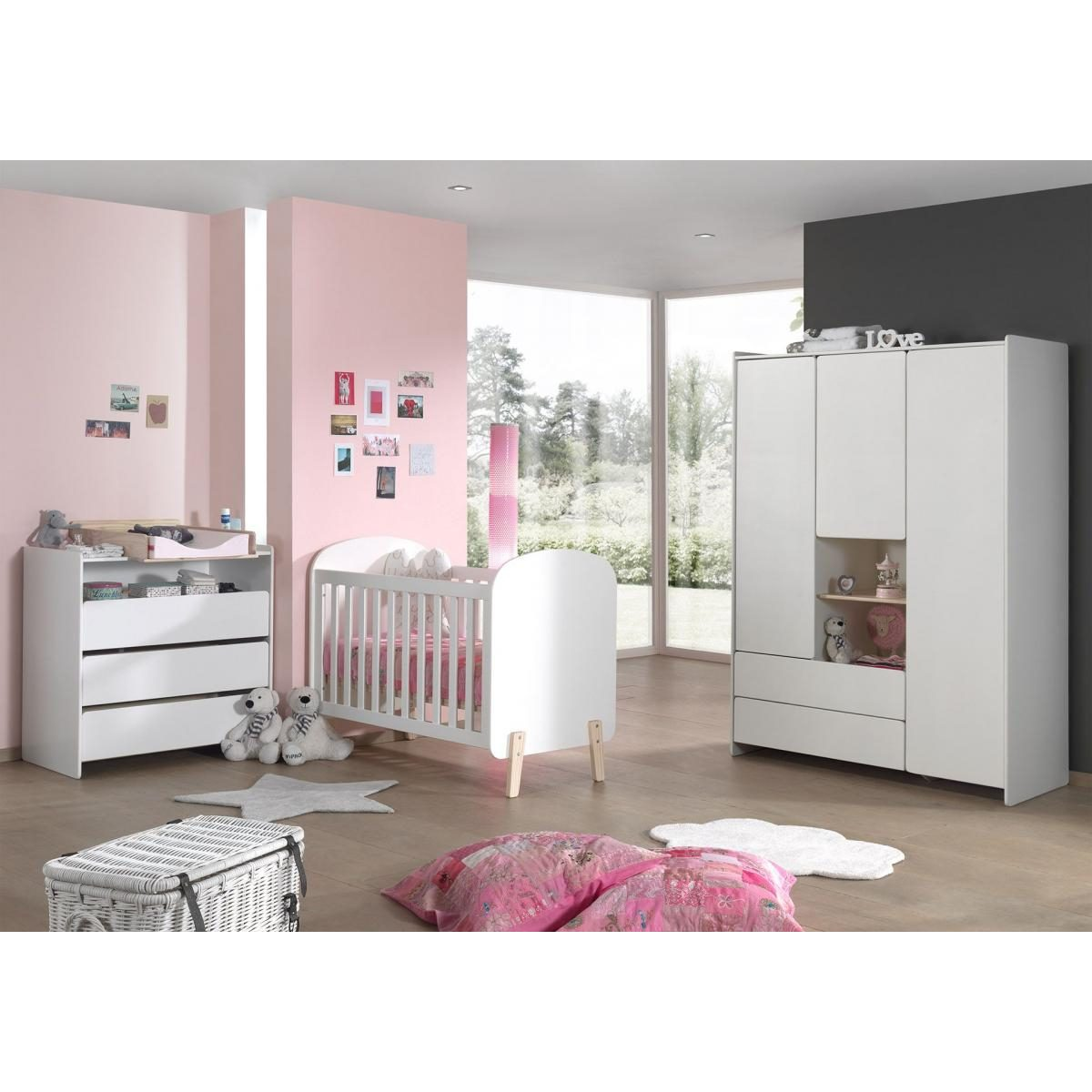 Ein Kinderzimmer mit rosa Wänden, weißem Gitterbett, Kommode, Kleiderschrank und Spielzeug auf dem Holzboden.