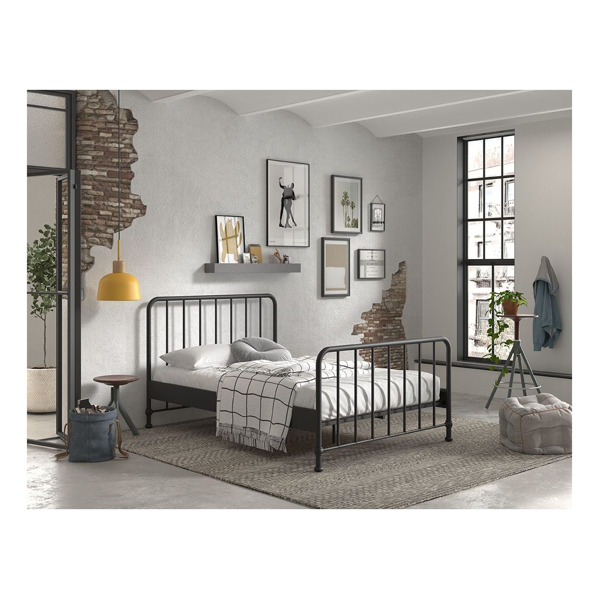Ein schwarzes Metallbett in einem Loft-Schlafzimmer mit Backstein, Bildern, gelber Lampe und großem Fenster.