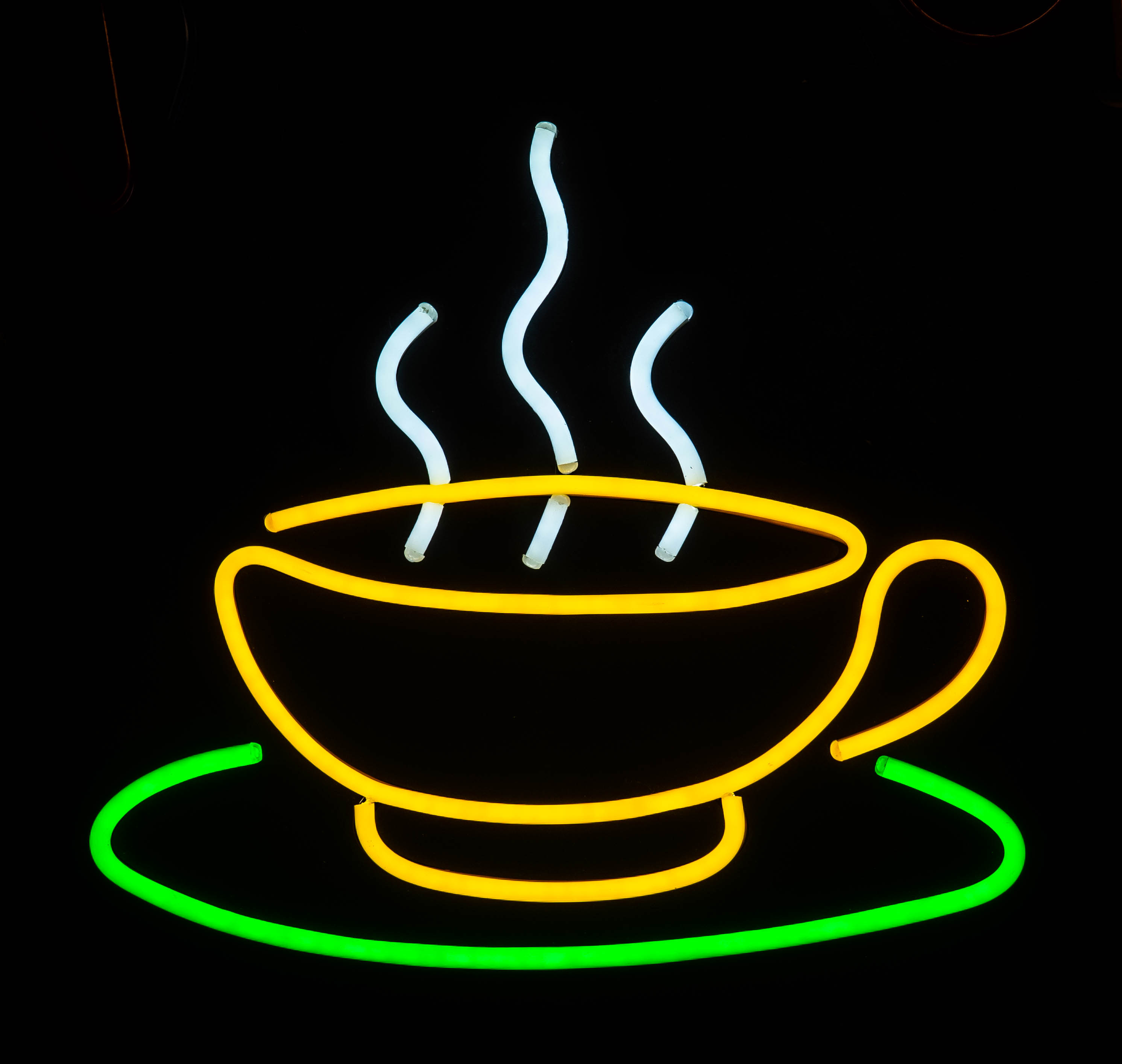 Ein gelbes Neon-Kaffeetassen-Schild mit grünem Untersetzer und weißem Dampf auf schwarzem Grund.