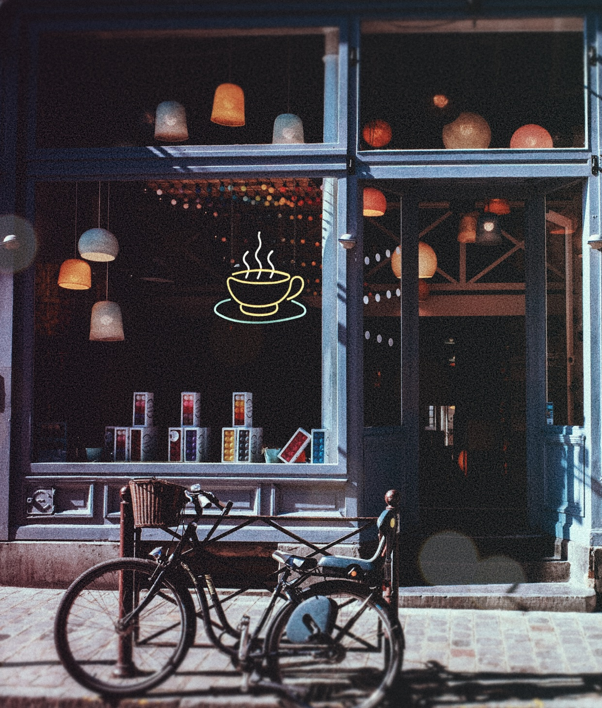 Ein Fahrrad steht vor einem gemütlichen Café mit einem leuchtenden Neon-Kaffeetassenschild und Lampen.