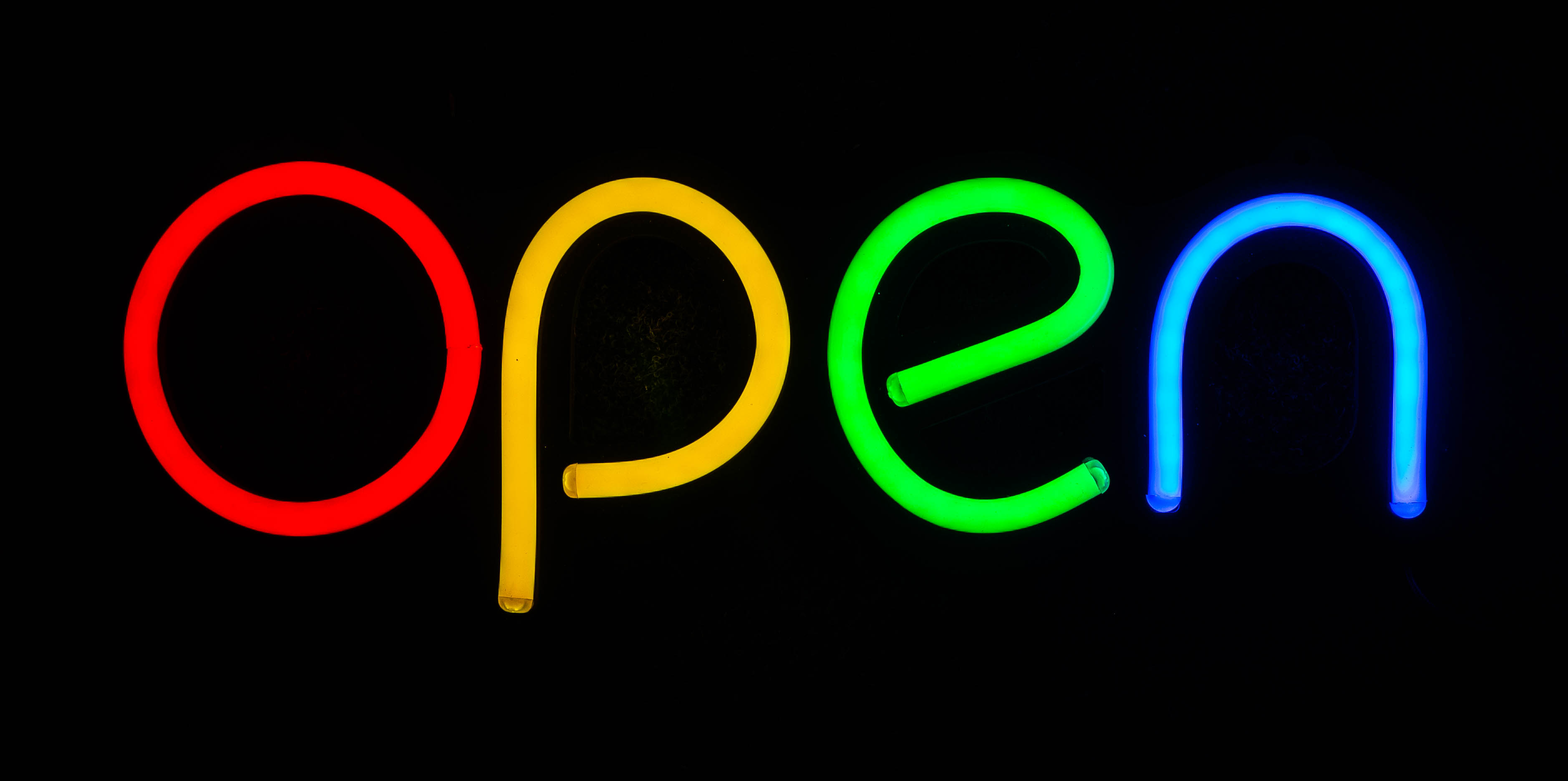 Ein farbigen Neon-Schriftzug mit dem Wort OPEN auf schwarzem Hintergrund.