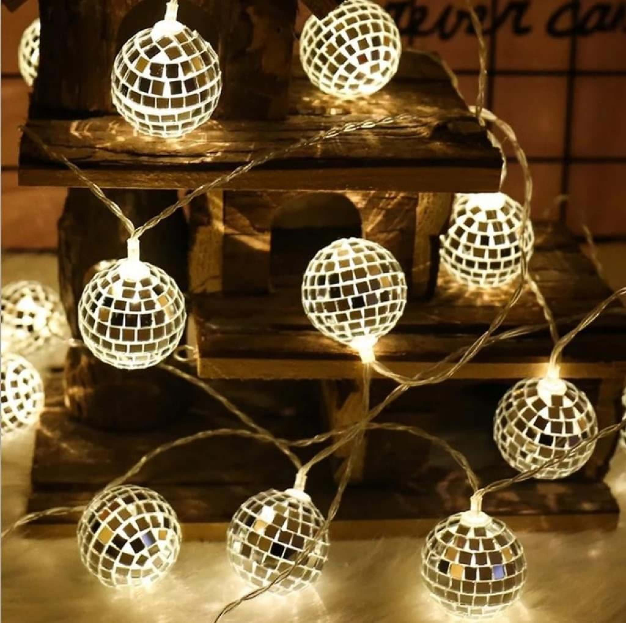 Leuchtende Mosaik-Diskokugel-Lichterkette vor einer rustikalen Holzstruktur.