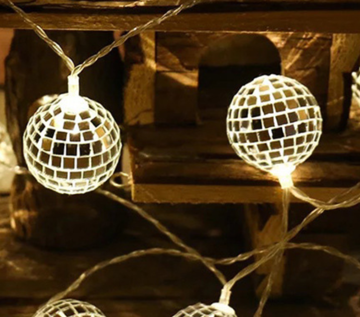Beleuchtete Spiegelkugel-Lichterkette hängt vor einem hölzernen Hintergrund.