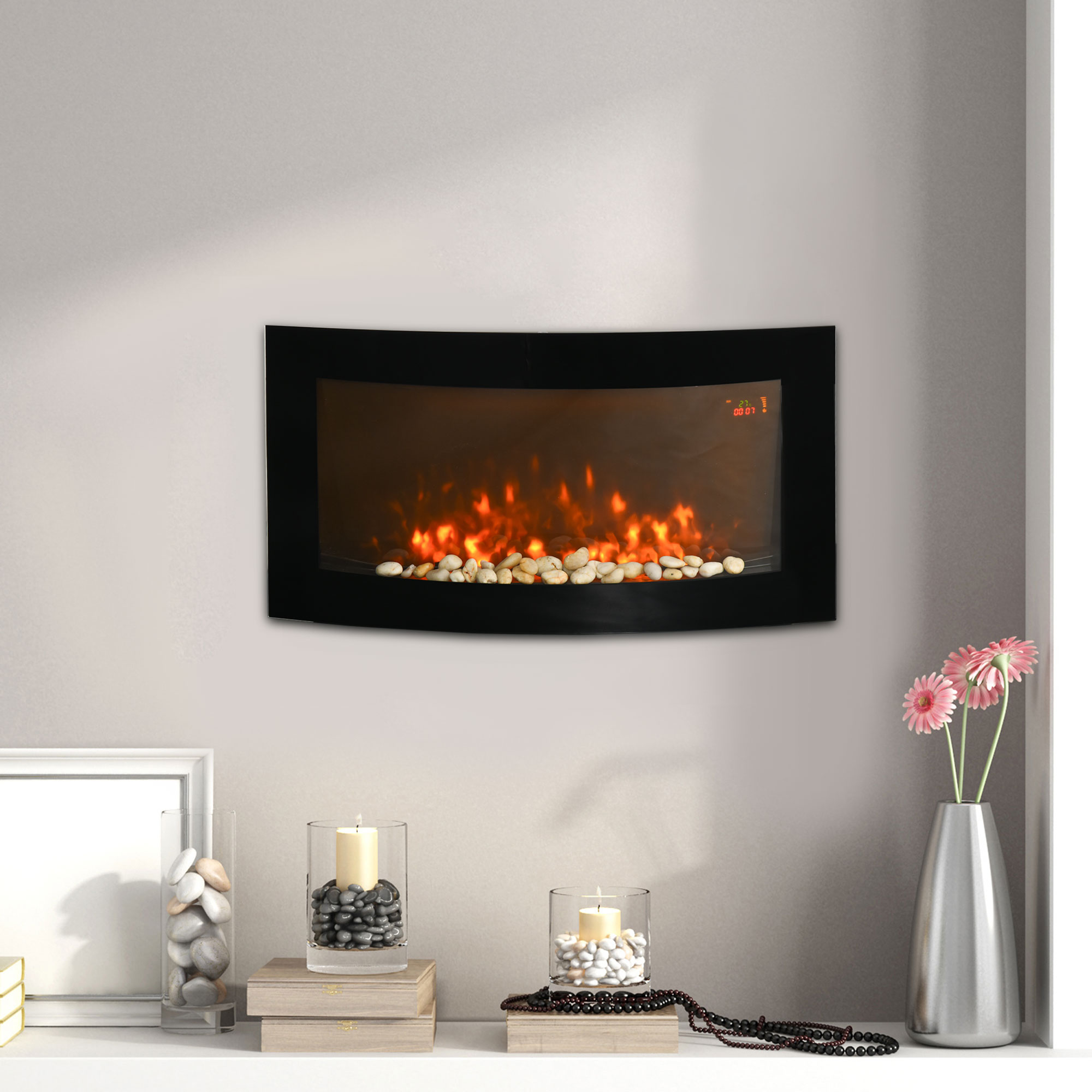 Chimenea eléctrica de pared con fuego artificial, decorada con velas, piedras y flores rosas en un florero.