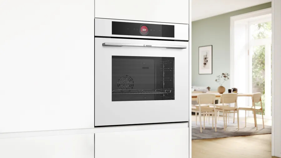 Un moderno forno da incasso bianco in una parete della cucina, con zona pranzo sullo sfondo.