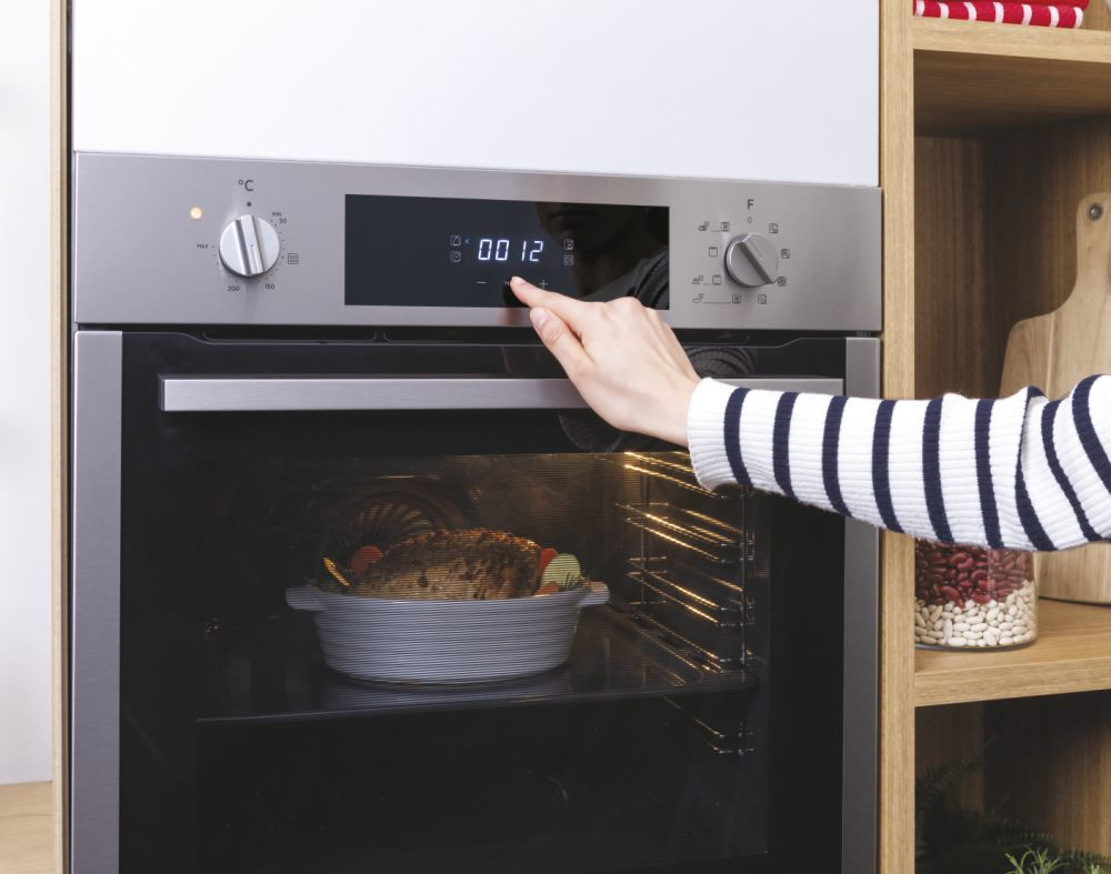 Una mano con un maglione a righe imposta il timer su un forno moderno con una teglia all'interno.