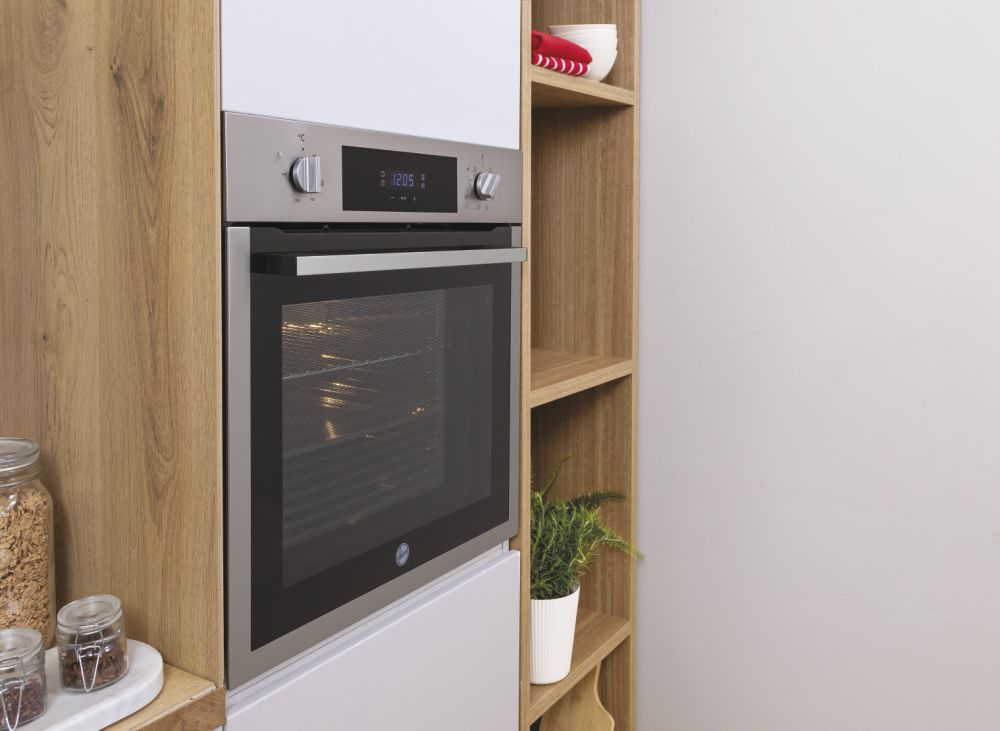 Un forno a incasso in acciaio inox in una cucina in legno con mensole, barattoli e una pianta.