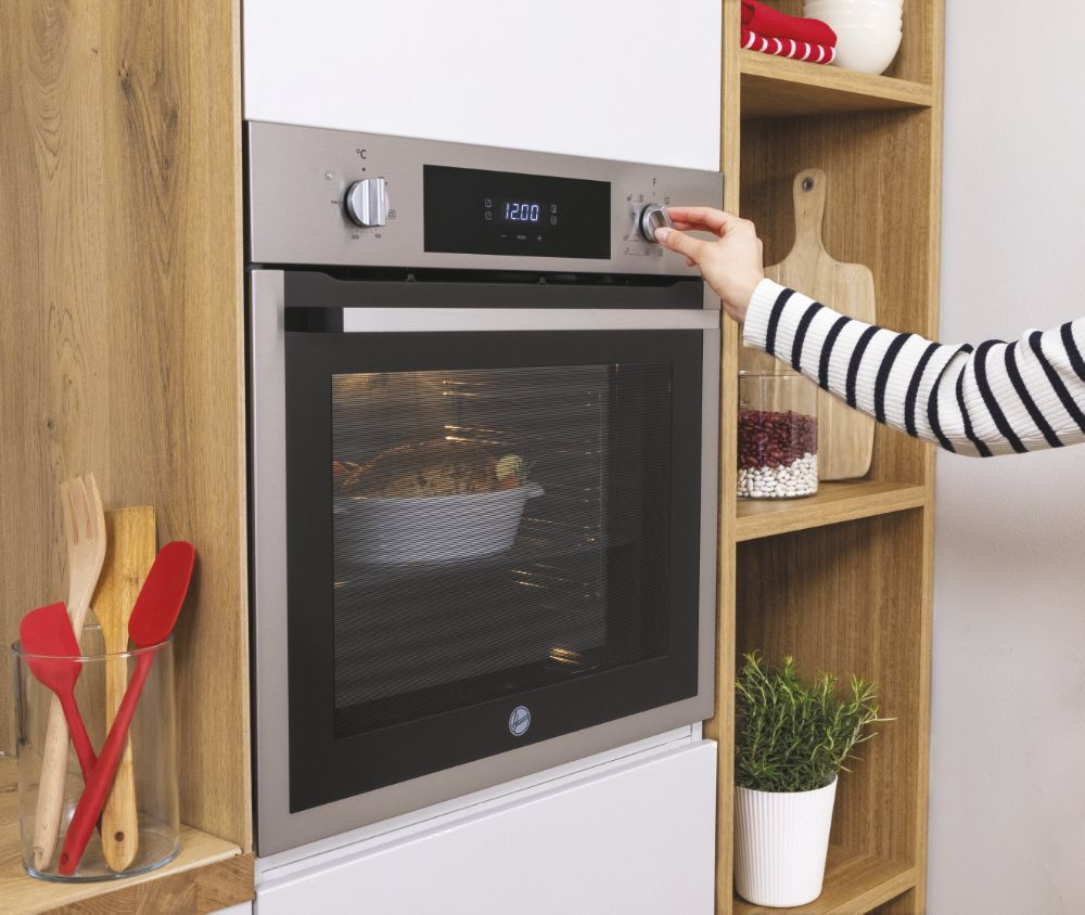 Una mano gira la manopola di un forno in acciaio inossidabile in mobili di legno.