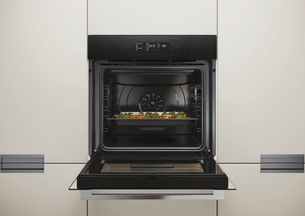 Un forno incassato nero con lo sportello aperto e una teglia di verdure arrostite.