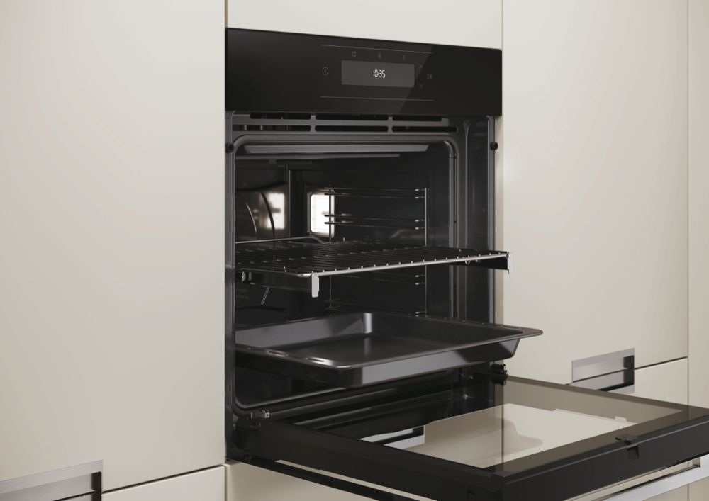 Un forno nero da incasso moderno e aperto con una griglia e una teglia in un mobile da cucina chiaro.