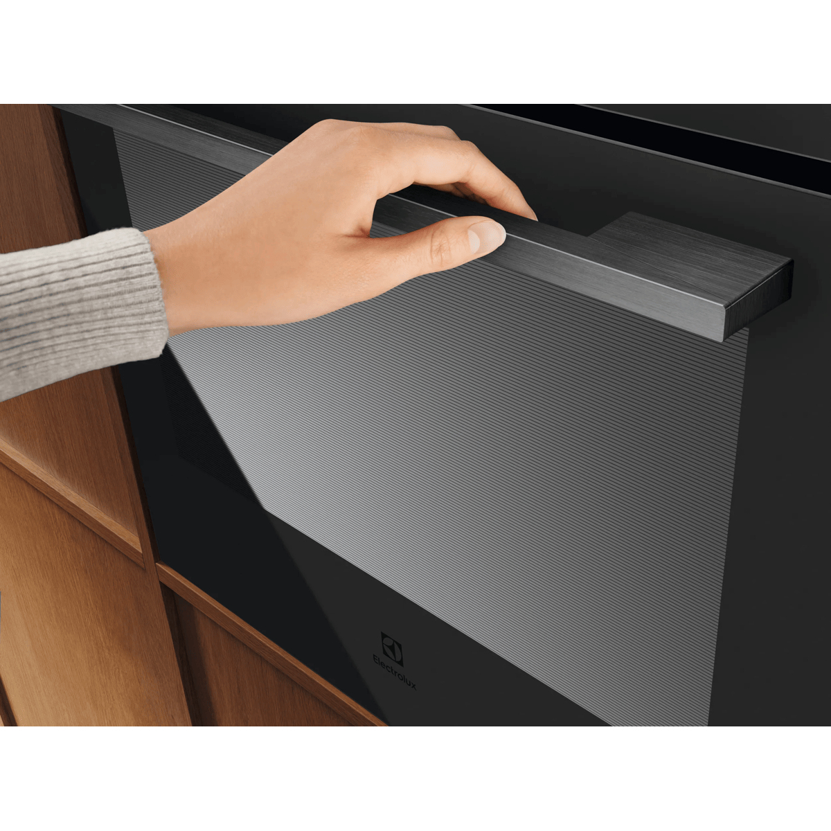 Una mano apre la porta di un forno nero Electrolux in mobili in legno.