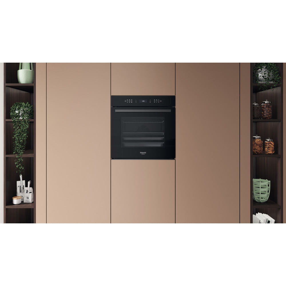 Un forno da incasso nero su parete beige, affiancato da ripiani scuri con piante e barattoli.