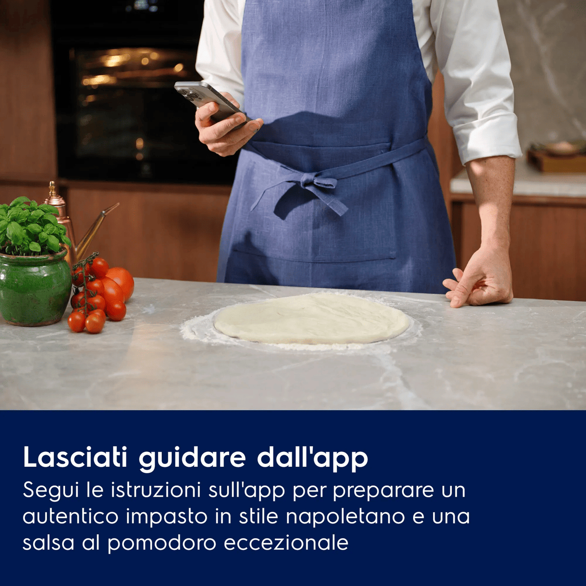 Persona con grembiule blu usa lo smartphone vicino a impasto per pizza e pomodori.
