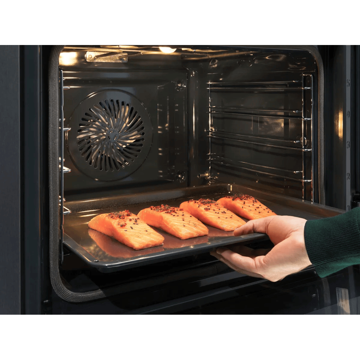 Una mano inserisce una teglia con quattro filetti di salmone nel forno.
