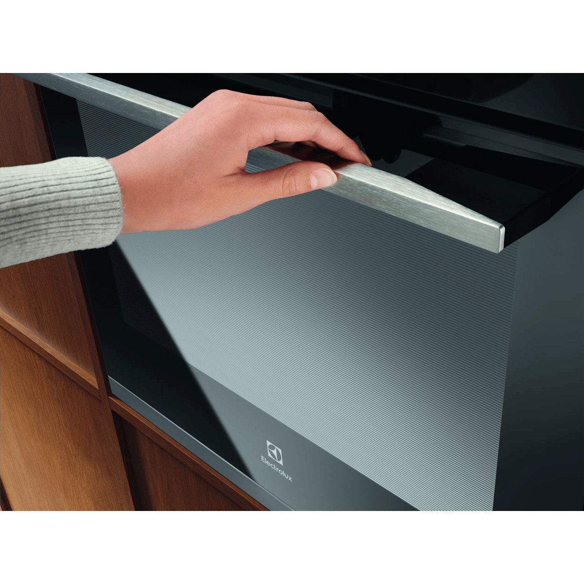 Una mano apre la porta con maniglia in acciaio inossidabile di un moderno forno Electrolux nero.