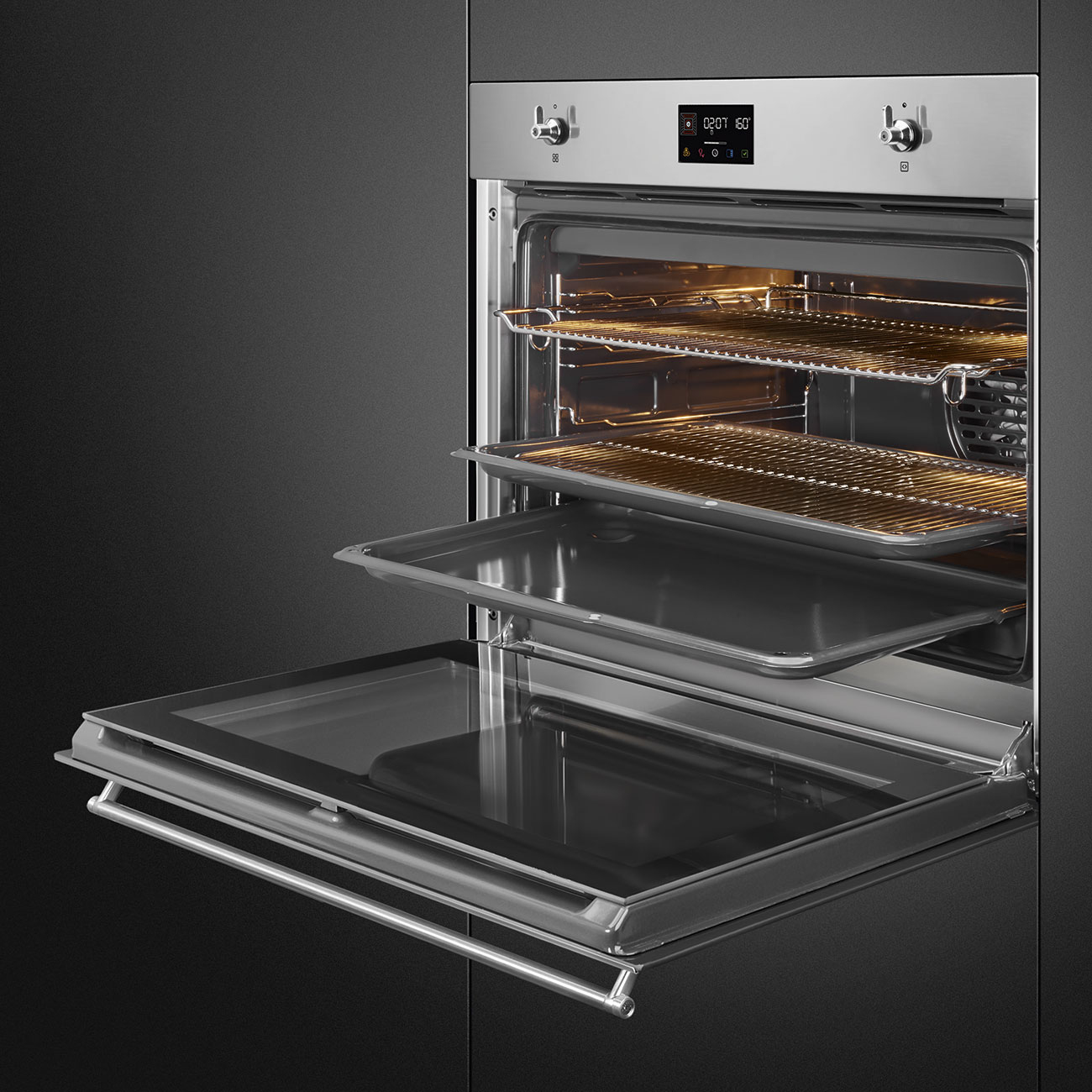 Forno da incasso argentato aperto con interno illuminato, griglie e teglie su sfondo scuro.