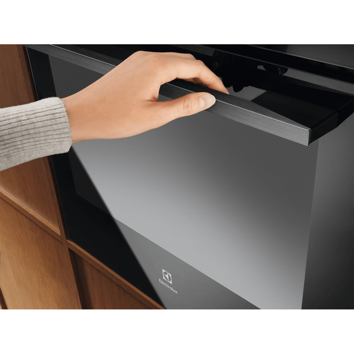 Una mano apre la porta nera di un forno Electrolux.