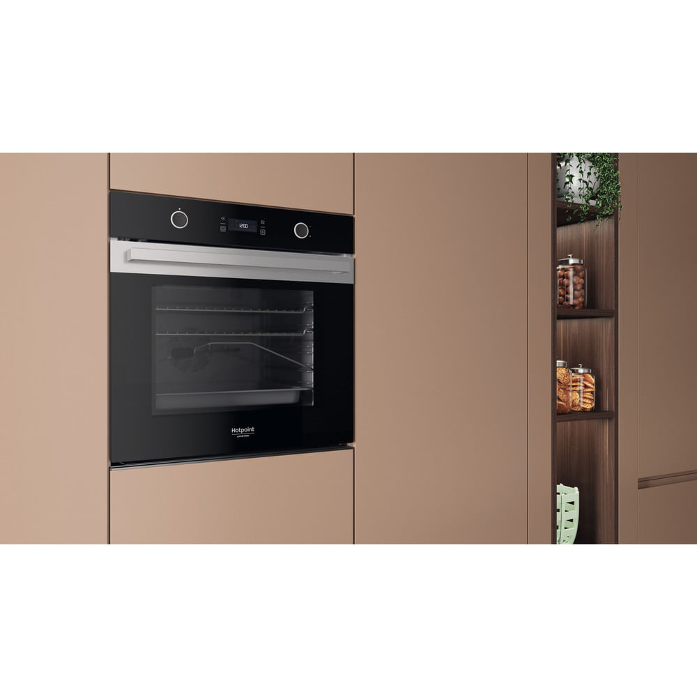 Un forno Hotpoint nero e argento integrato in mobili da cucina beige con una libreria vicina.