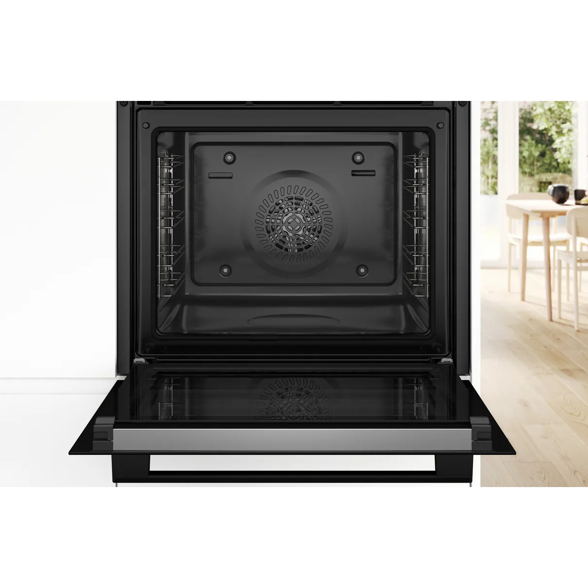 Un forno da incasso nero aperto con interno vuoto mostra la ventola di ventilazione, con una cucina luminosa sullo sfondo.