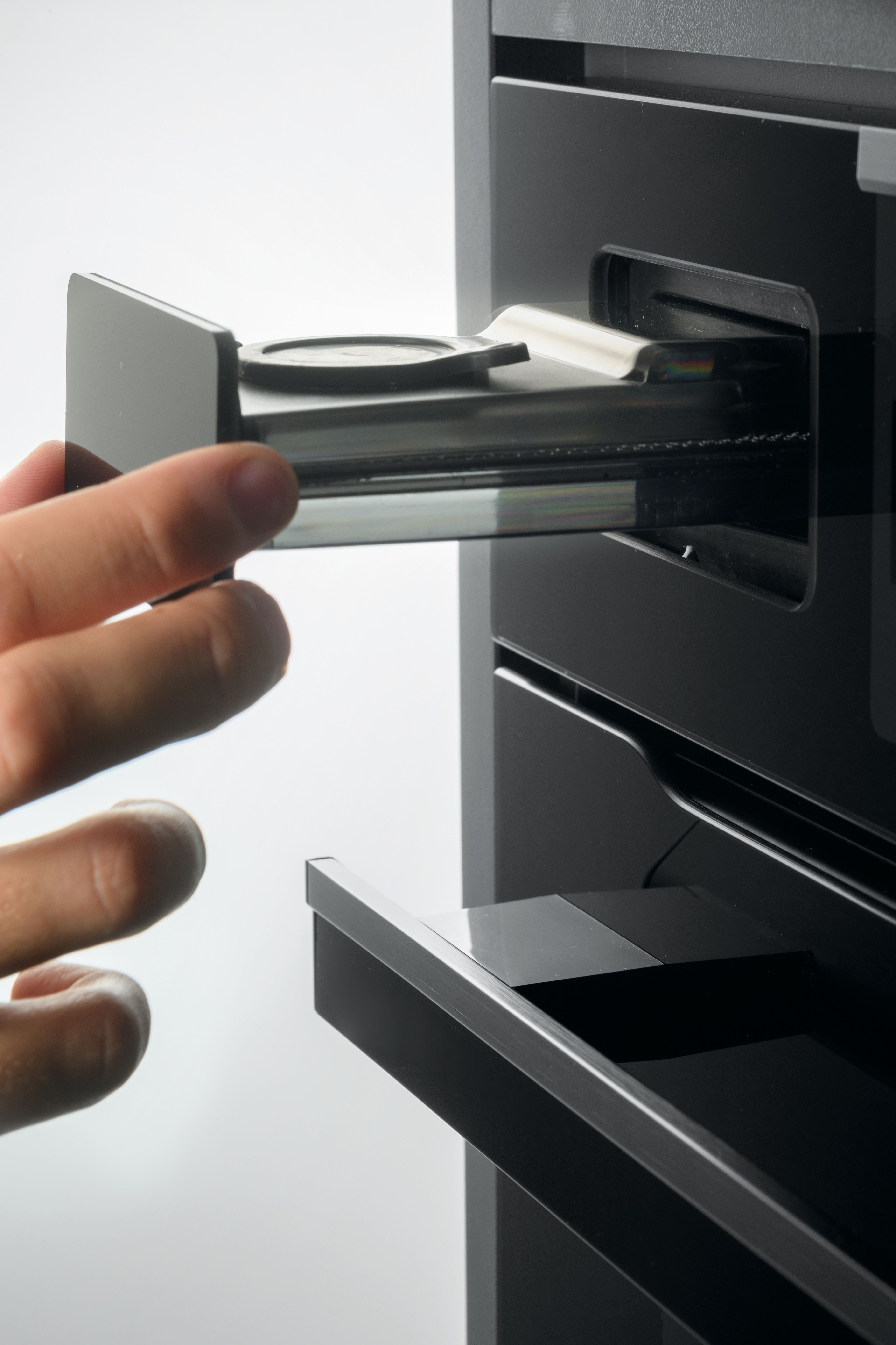 Una mano estrae un cassetto nero piatto da una macchina da caffè.