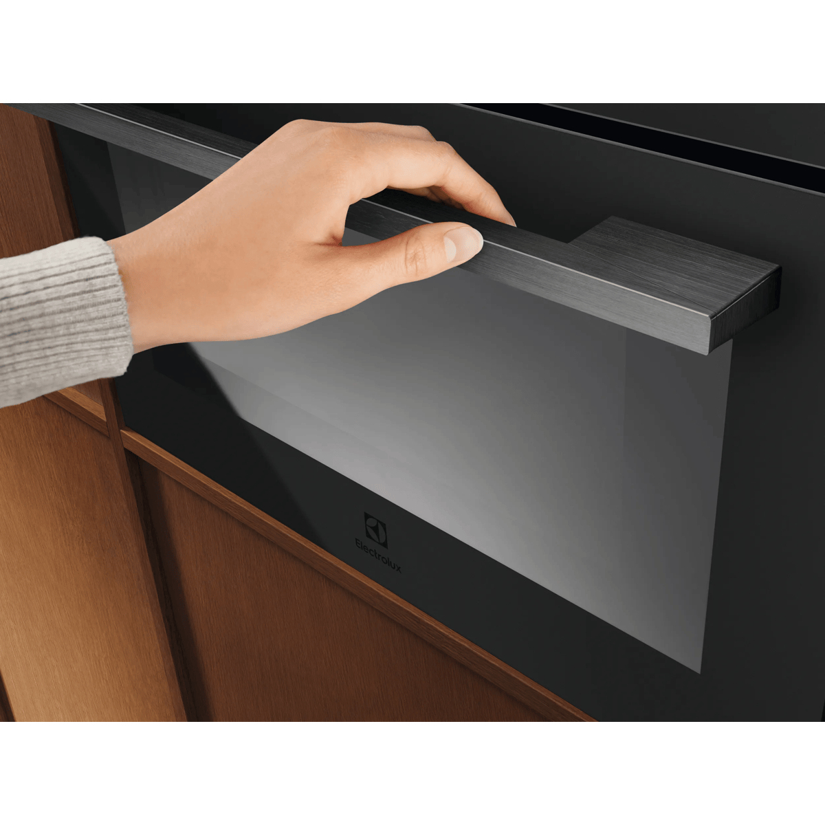Una mano apre la porta nera di un moderno forno Electrolux davanti a mobili in legno.